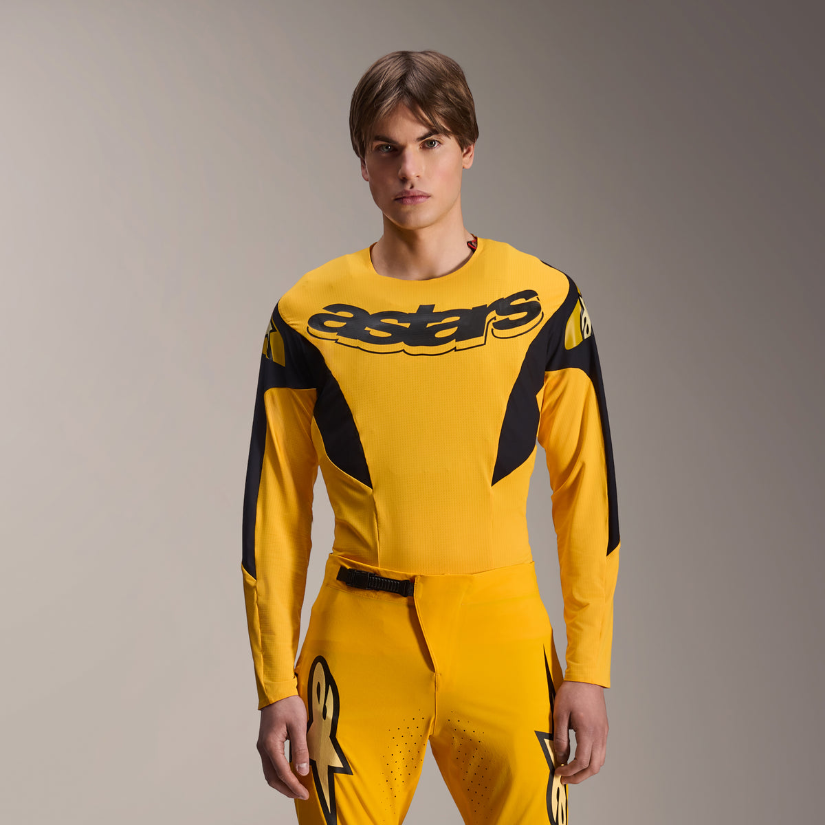Alpinestars Limited Edition A-Supra Melt Gold uitrustingsset, geel MTB-fietsshirt met lange mouwen en bijpassende broek, zwarte Astars-branding op de borst, sportieve performance-pasvorm voor mountainbiken, model draagt de volledige uitrusting