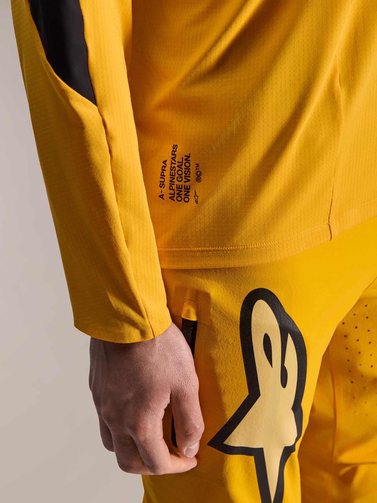 Alpinestars Limited Edition A-Supra Melt Gold Gear-Set, close-up van een donkergele jersey met lange mouwen en bijpassende broek, met 'One Goal. One Vision.' branding en een groot Astars-logo, micro-geperforeerd technisch materiaal voor MTB-races