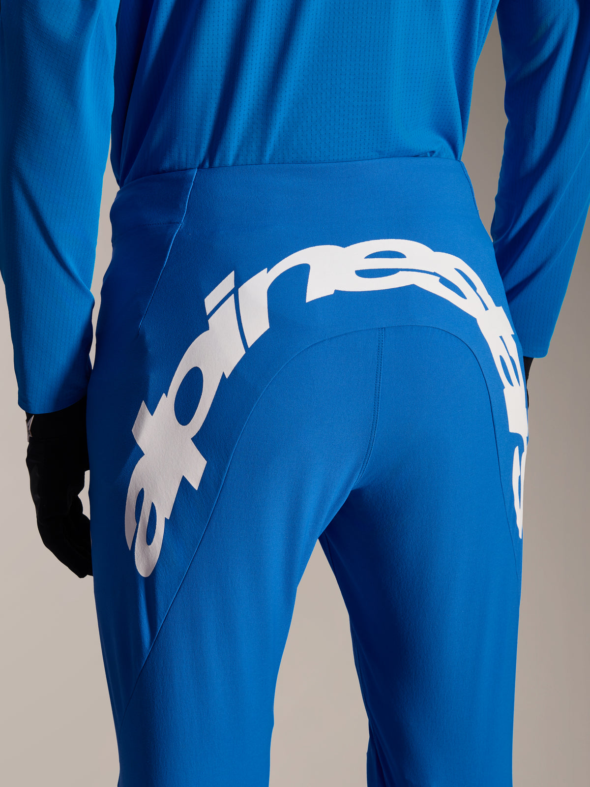 Alpinestars A-Supra Melt broek en jersey, blauwe MTB-uitrusting, achteraanzicht met een groot wit Alpinestars-woordmerk op het achterjuk van de broek, bijpassende jersey met lange mouwen en zwarte handschoenen