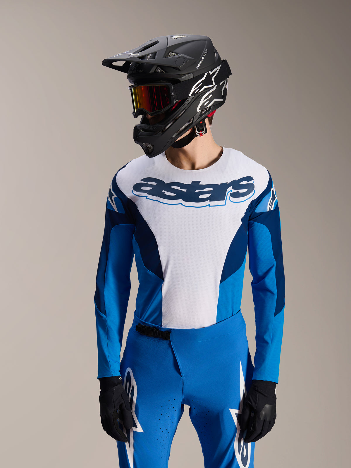 Model trägt Alpinestars A-Supra Melt Langarm-Trikot in Blau und Weiß mit 'astars'-Wortmarke auf der Brust, kombiniert mit passender blauer MTB-Hose, schwarzem Fullface-Helm und Goggle, komplette Mountainbike-Rennausrüstung.