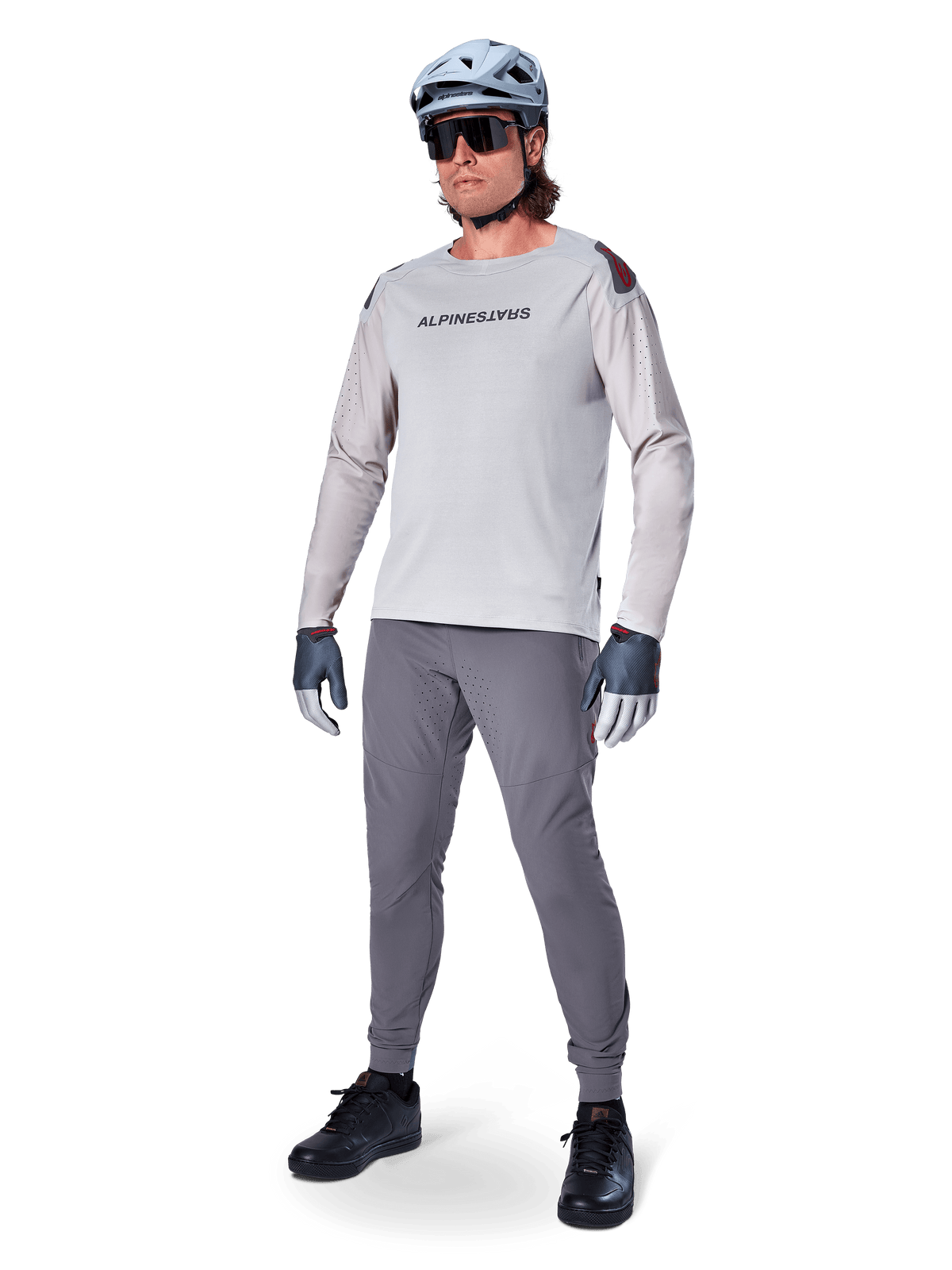 Alpinestars A-Aria Polartec Switch Jersey, Langarm-MTB-Trikot, Hellgrau, getragen mit dunkelgrauer Mountainbike-Hose, Helm und Handschuhen, mit laserperforierten Ärmeln und Alpinestars-Logo auf der Brust.