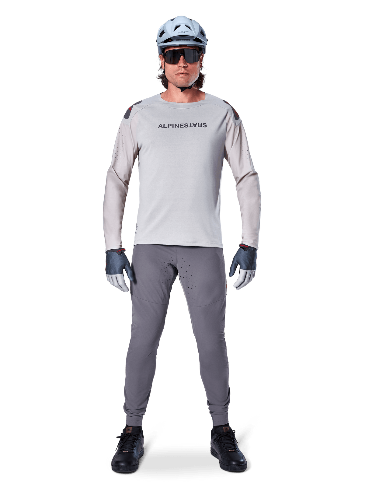 Alpinestars A-Aria Polartec Switch Langarmtrikot, Hellgrau, getragen von einem männlichen Mountainbike-Fahrer mit dunkelgrauer MTB-Hose, hellblauem Helm und Sonnenbrille, mit Markenlogo auf der Brust und laserperforierter Belüftung an den Ärmeln, komplette Offroad-Radsportausrüstung.