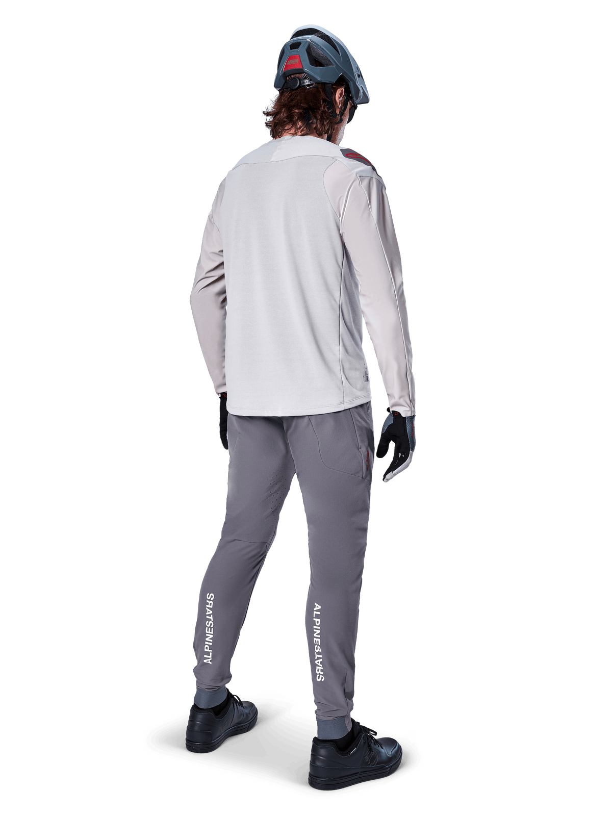 Rückansicht eines Radfahrers im Alpinestars A-Aria Polartec Switch Langarmtrikot in Hellgrau, kombiniert mit einer dunkelgrauen Mountainbike-Hose mit weißem Alpinestars-Branding an den Waden, schwarzen Handschuhen und einem grauen Helm.