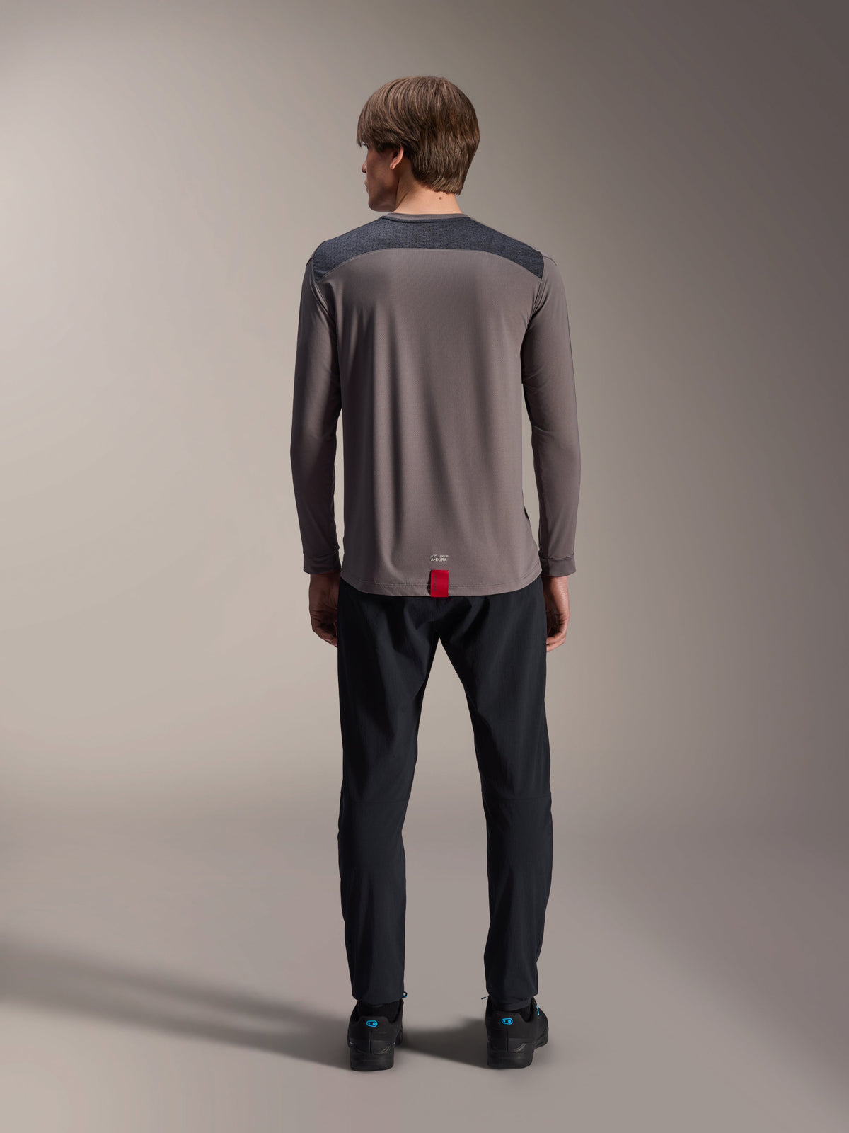 Alpinestars A-Dura Insert Astar jersey met lange mouwen in donkergrijs, achteraanzicht, met antracietkleurige schouderpanelen en een rood label aan de zoom, gedragen met een zwarte broek en schoenen, mountainbike performance kleding