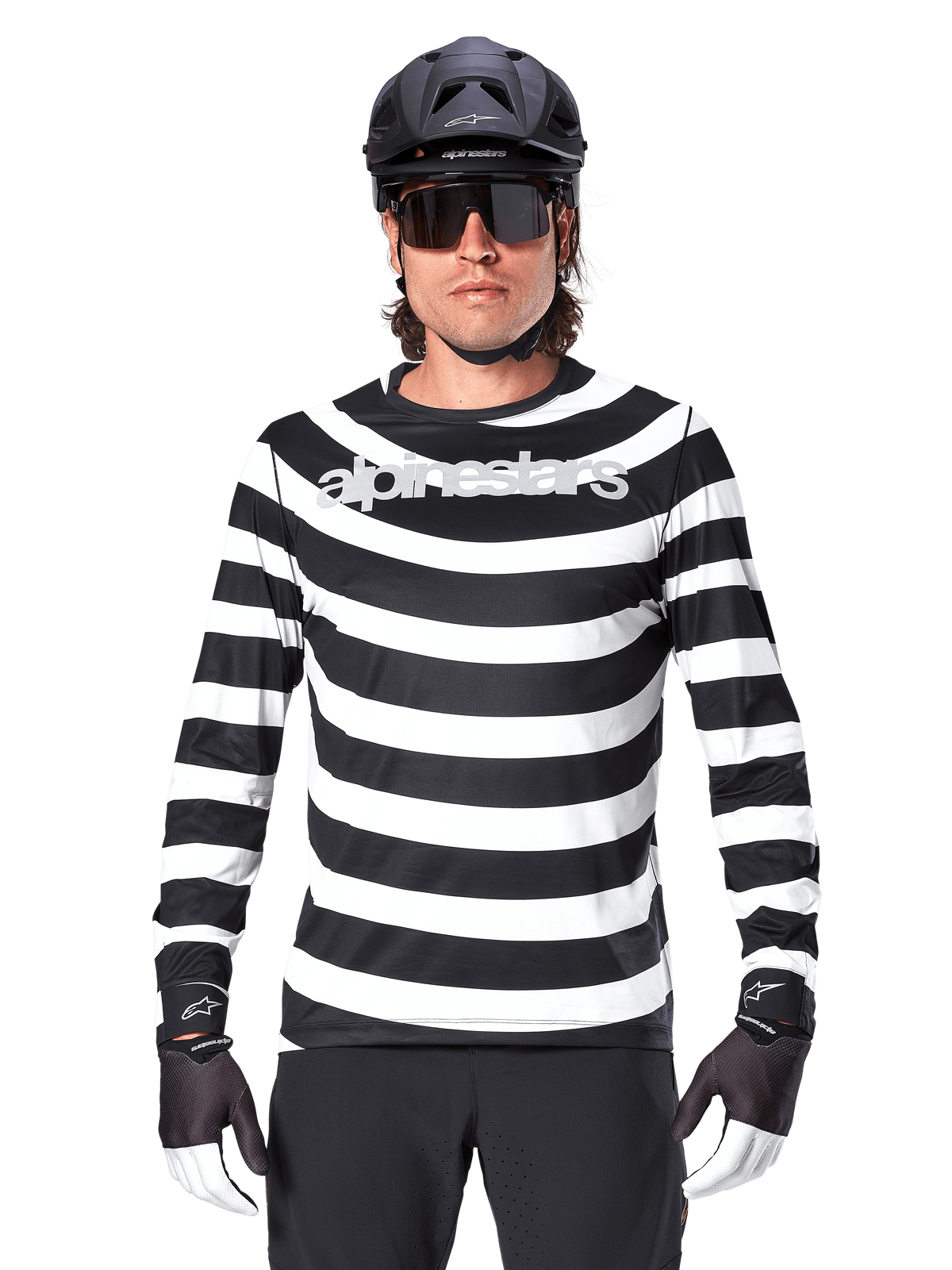 Alpinestars A-Aria Oscar Jersey met lange mouwen, zwart-wit horizontaal gestreept, reflecterend Alpinestars-logo op de borst, mannelijke fietser met zwarte MTB-helm, fietszonnebril en performance handschoenen