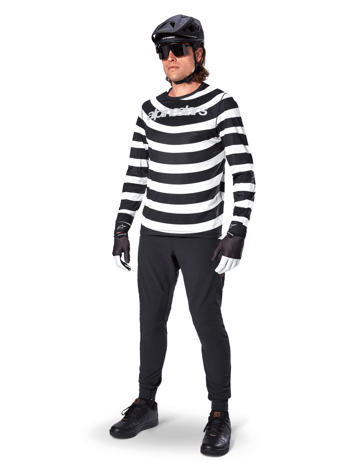 Alpinestars A-Aria Oscar Jersey met lange mouwen, zwart en wit met opvallende horizontale spiraalvormige strepen, wit gebogen Alpinestars-logo, performance MTB-kleding gedragen met zwarte fietsbroek en helm