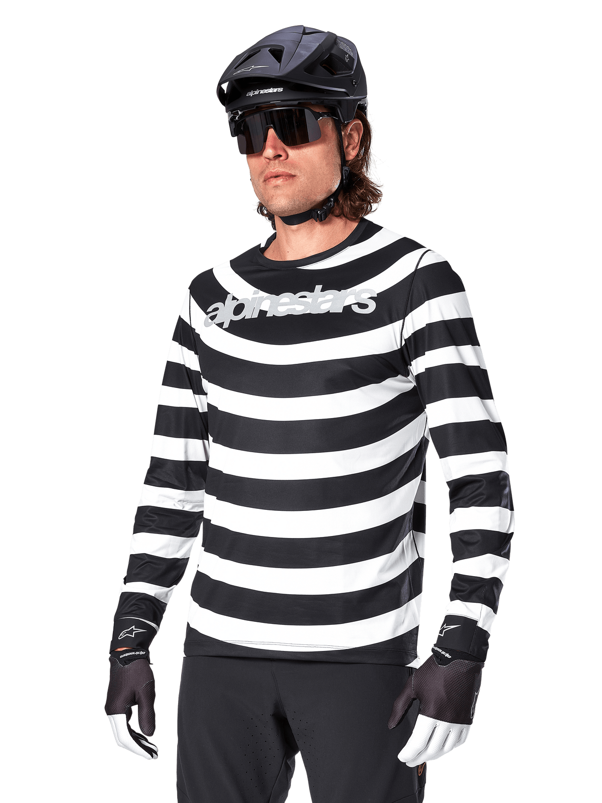 Alpinestars A-Aria Oscar Jersey met lange mouwen, MTB-wielershirt, zwart-witte horizontale strepen, gedragen met een zwarte helm en zonnebril, voorzien van Alpinestars-branding op de borst, technische mountainbike-kleding