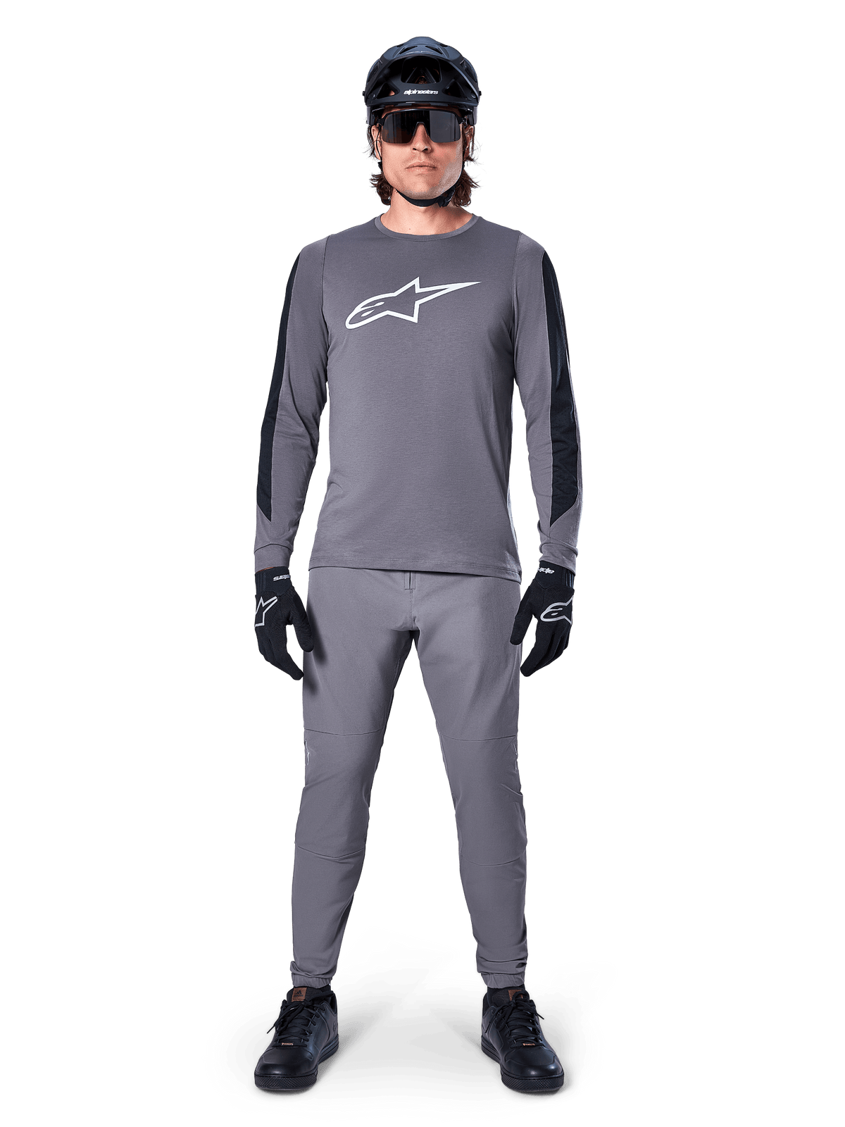 Alpinestars A-Dura Dri Astar Jersey, langärmeliges MTB-Trikot in Dunkelgrau, mit weißem Brustlogo und schwarzen Ärmeleinsätzen, getragen mit passender grauer Hose, schwarzem Helm, Sonnenbrille und Handschuhen für ein komplettes Offroad-Radsport-Outfit
