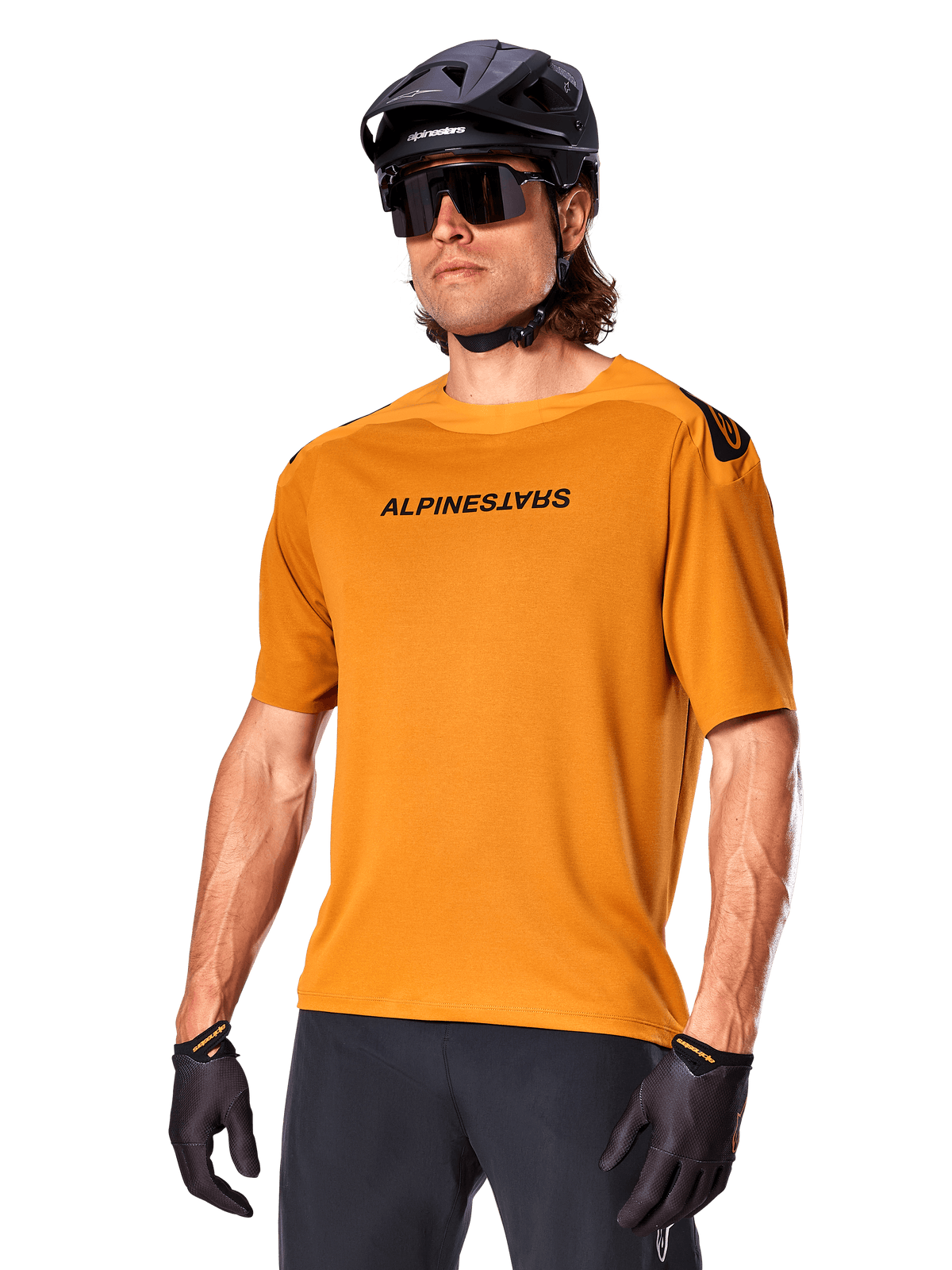 Maillot Alpinestars A-Aria Polartec Switch, maillot de VTT à manches courtes, or foncé avec marquage noir, porté par un mannequin avec casque noir, lunettes de soleil et gants de cyclisme, vêtement de VTT haute performance