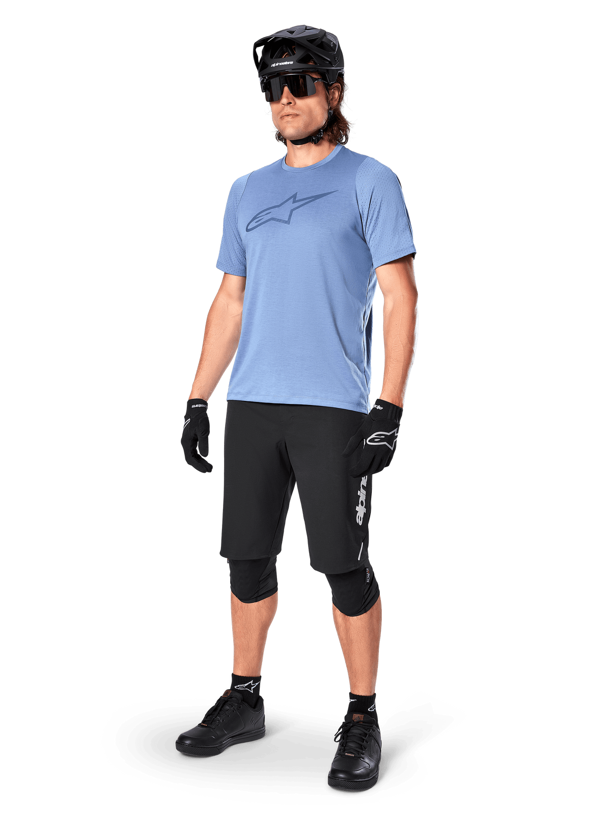 Mannelijke rijder draagt de Alpinestars A-Dura Dri Astar jersey met korte mouwen in Infinity Blue, gecombineerd met een zwarte MTB-short, zwarte helm, zonnebril, kniebeschermers en handschoenen, complete mountainbike-outfit