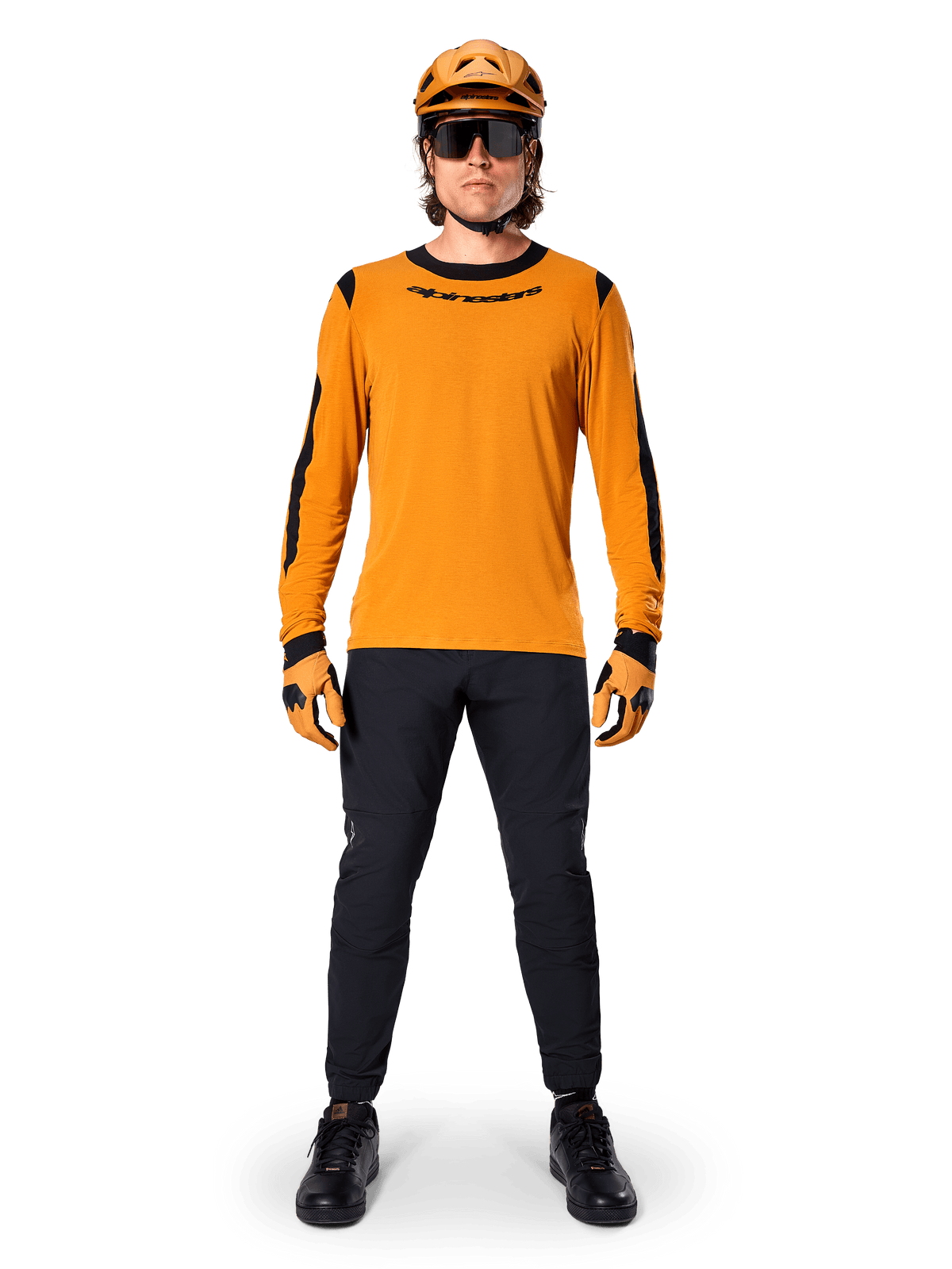 Vététiste portant le maillot à manches longues Alpinestars A-Dura Dri Wool, or foncé avec des accents noirs au col et aux manches, associé à un pantalon noir, casque et gants dorés assortis, lunettes de soleil noires, équipement de VTT professionnel