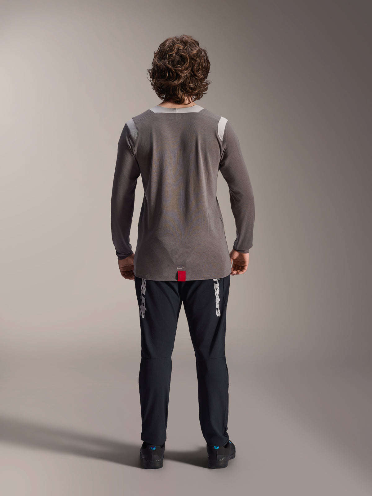 Alpinestars A-Dura Elite Hose und A-Dura Dri Wool Langarmtrikot, schwarze Hose mit weißem Branding, graues technisches Trikot, Rückansicht eines Mountainbike-Outfits, strapazierfähige Offroad-Radsportbekleidung