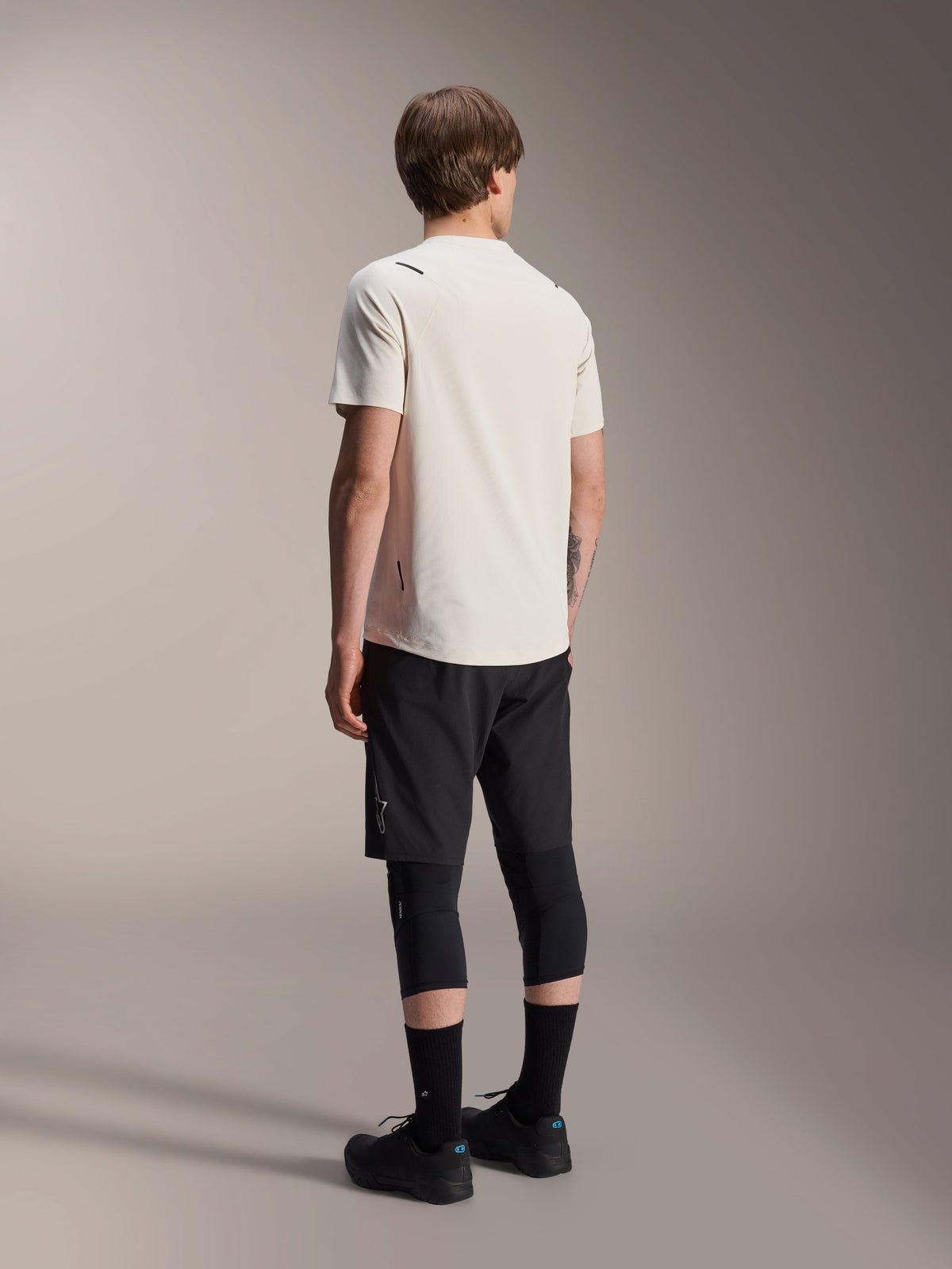 Maillot Alpinestars A-Aria Astar, maillot de VTT à manches courtes, écru, vue arrière montrant la coupe performance et la queue de pie plus longue, associé à un short de VTT noir, des genouillères et des chaussures de vélo noires pour les sessions de VTT.