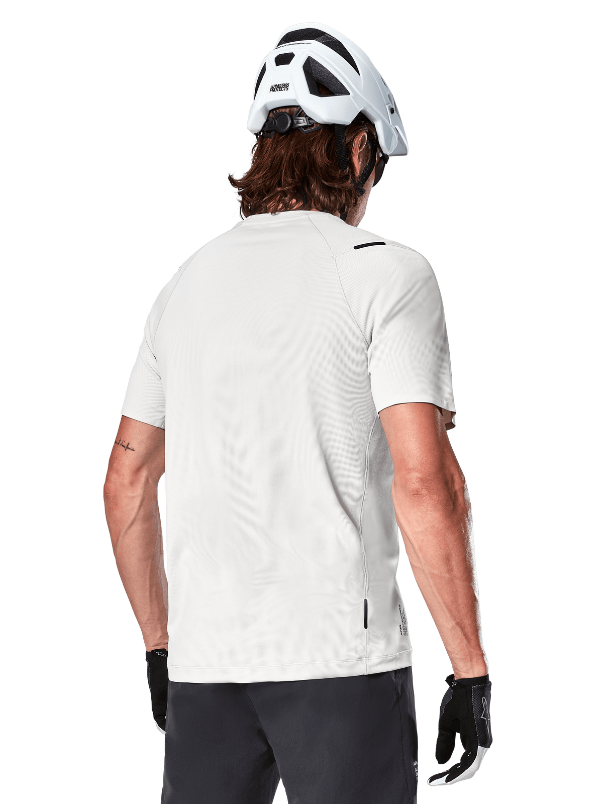 Alpinestars A-Aria Astar Jersey, korte mouwen, White Dove, achteraanzicht van lichtgewicht ademende mountainbike jersey, gedragen met een witte helm en zwarte fietshandschoenen, met een verlengde achterkant voor extra dekking