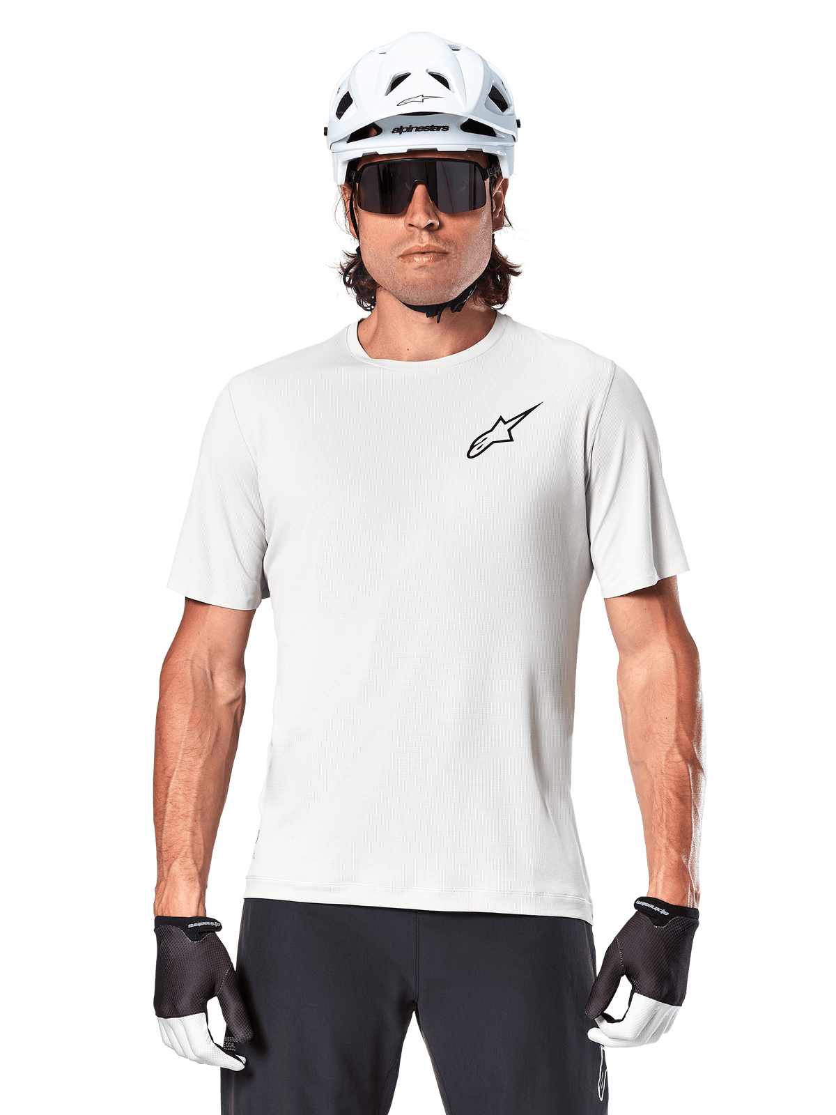 Fietser draagt Alpinestars A-Aria Astar Jersey met korte mouwen, White Dove met klein zwart Astar-logo op de borst, witte fietshelm, zwarte zonnebril en zwart-witte handschoenen, technische MTB-uitrusting voor off-road rijden