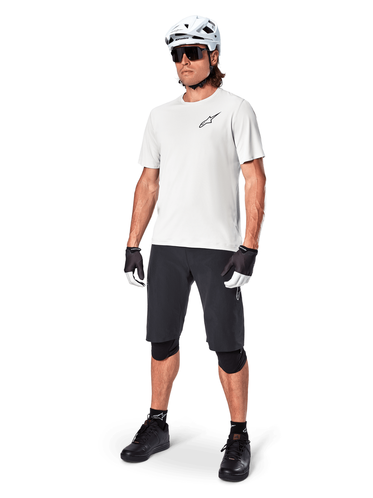 MTB-fietser die een Alpinestars A-Aria Astar Jersey met korte mouwen in White Dove draagt, gecombineerd met een zwarte mountainbike-short, witte helm en zwarte kniebeschermers, voorzien van een klein zwart logo op de borst, gecoördineerde fietsuitrusting voor trailprestaties