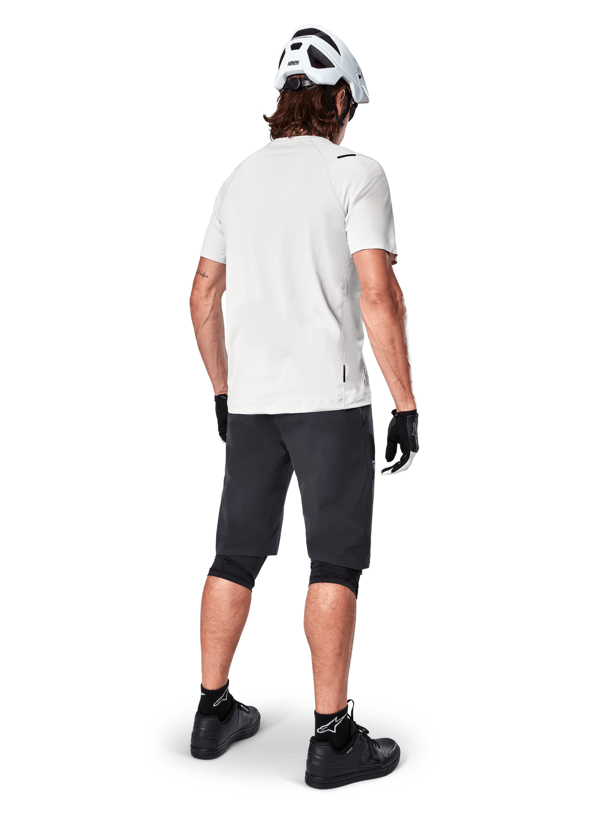 Wielrenner draagt het Alpinestars A-Aria Astar jersey met korte mouwen in White Dove, achteraanzicht, gecombineerd met zwarte MTB-short, kniebeschermers en een witte helm, lichtgewicht en ademende kleding voor off-road mountainbiken