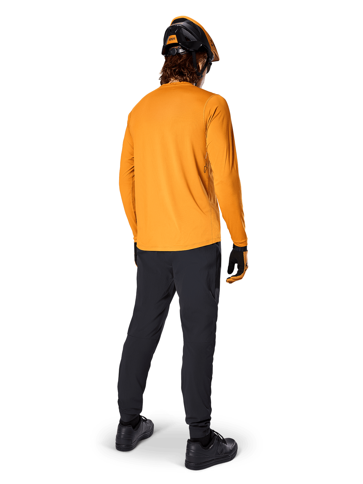 Cycliste de VTT vu de dos portant le maillot à manches longues Alpinestars A-Dura Rocker en Dark Gold, pantalon noir, casque orange et noir et chaussures noires, équipement de performance VTT coordonné pour le trail