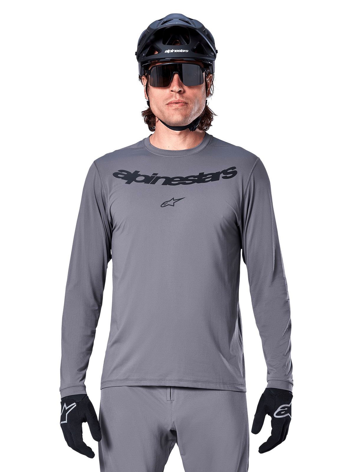 Cycliste portant le maillot à manches longues Alpinestars A-Dura Rocker, maillot de VTT gris foncé avec logo noir sur la poitrine, associé à un pantalon gris, un casque noir et des gants, conçu pour le cyclisme tout-terrain