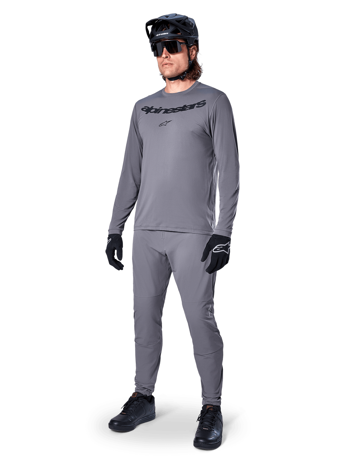 Maillot à manches longues Alpinestars A-Dura Rocker, gris foncé, porté par un mannequin avec un pantalon gris assorti, casque de VTT noir, lunettes de soleil et gants, style VTT décontracté pour la pratique du tout-terrain