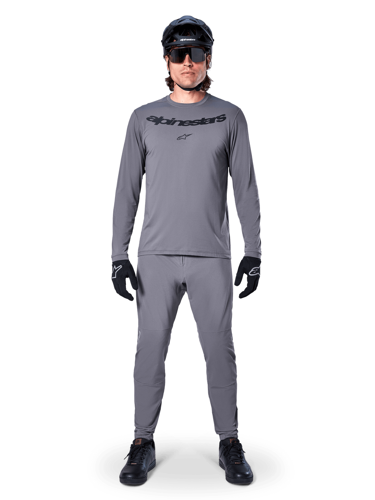 Cycliste masculin portant le maillot à manches longues Alpinestars A-Dura Rocker gris foncé, pantalon gris assorti, casque de VTT noir, lunettes de soleil et gants, équipement de VTT professionnel pour les sentiers tout-terrain