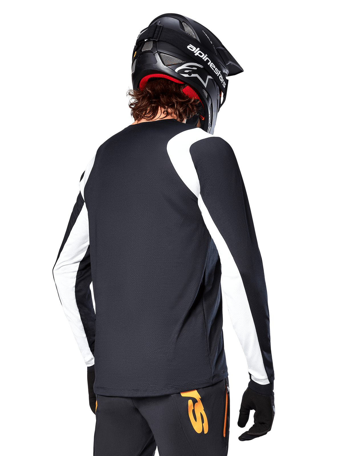 MTB-rijder draagt Alpinestars A-Supra Oscar jersey met lange mouwen, zwart met witte panelen op de schouders en mouwen, van achteren gezien, zwarte helm en handschoenen, broek met oranje accenten, duurzame off-road fietskleding