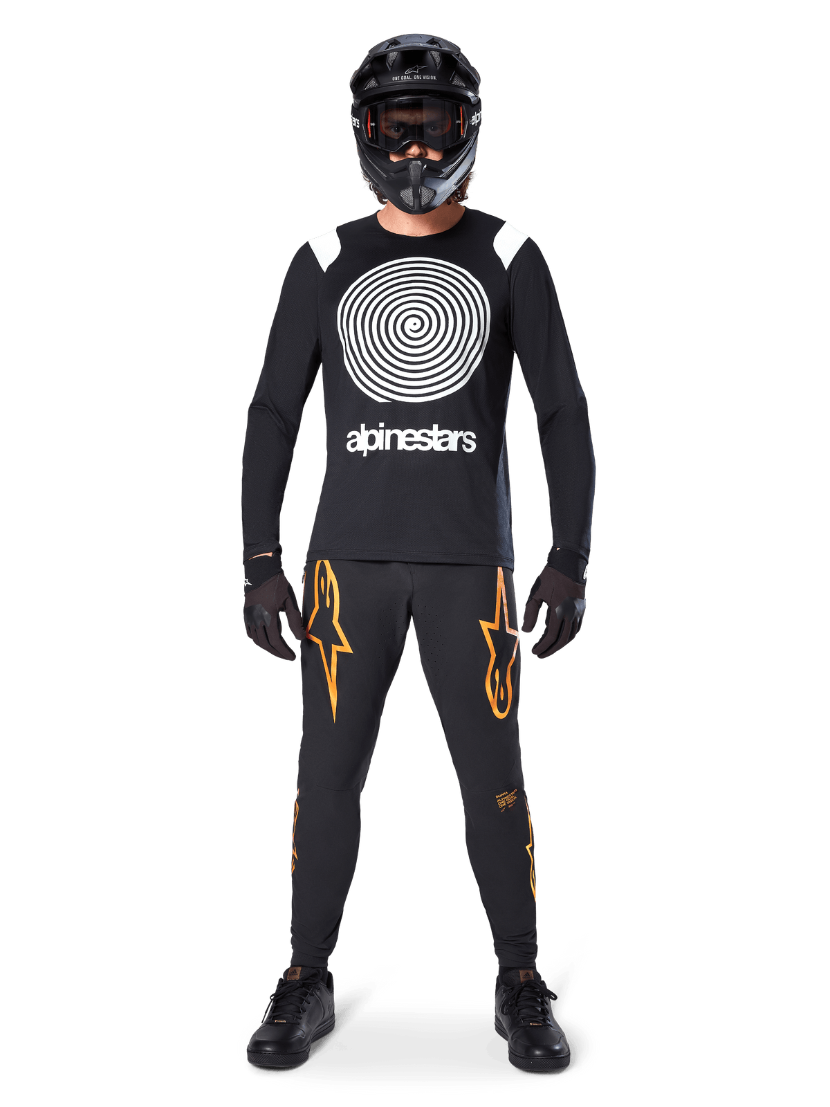 Mannelijk model in volledige mountainbike-uitrusting, Alpinestars A-Supra Oscar Jersey met lange mouwen in zwart met witte spiraalgrafiek op de borst, zwarte broek met oranje sterlogo's, zwarte full-face helm en bril, zwarte handschoenen en schoenen, gecoördineerde outfit voor MTB gravity riding