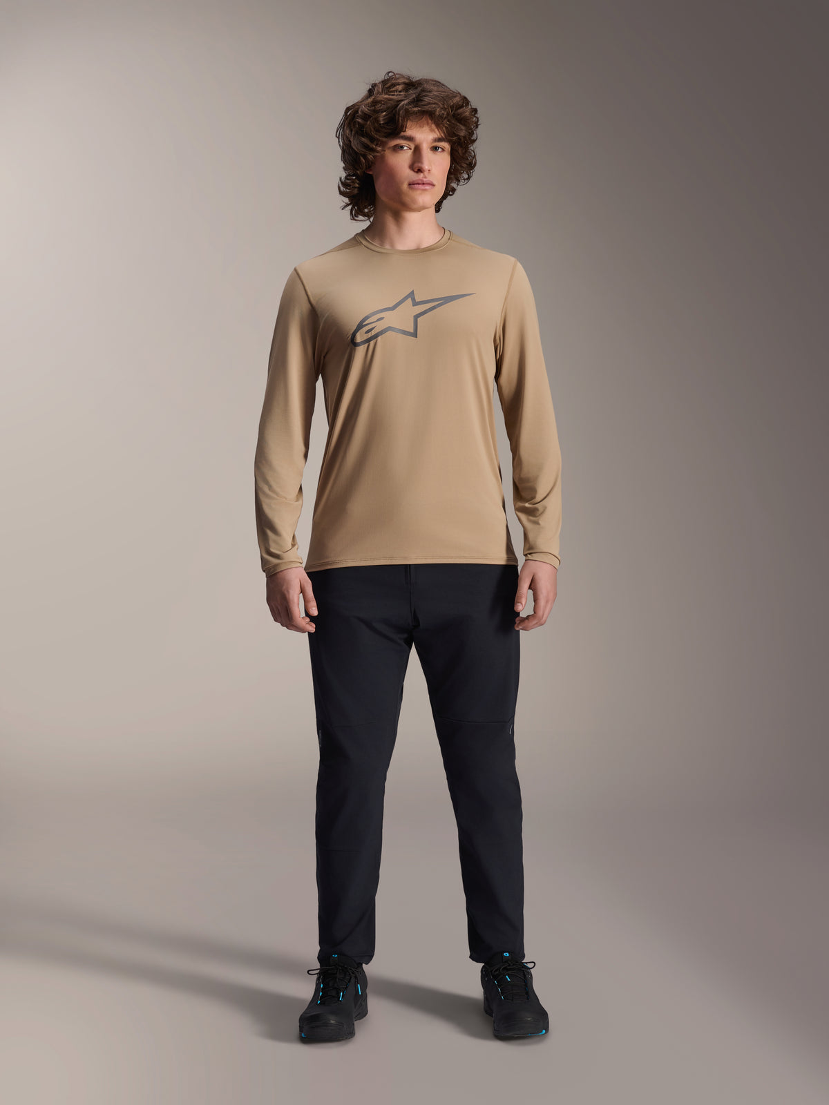 Alpinestars A-Dura Astar Long Sleeve Jersey, Light Brown with grey Astars chest logo, worn by a model with black technical pants and shoes, casual mountain bike performance gear