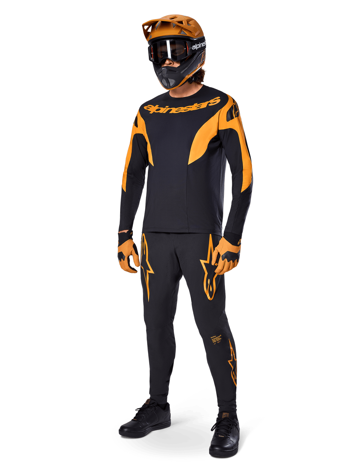 MTB rider wearing complete racing gear, Black A-Supra Race Jersey with orange accents, matching black pants with orange Alpinestars logos, orange and black full-face helmet with goggles, orange and black gloves, coordinated outfit for mountain bike racing