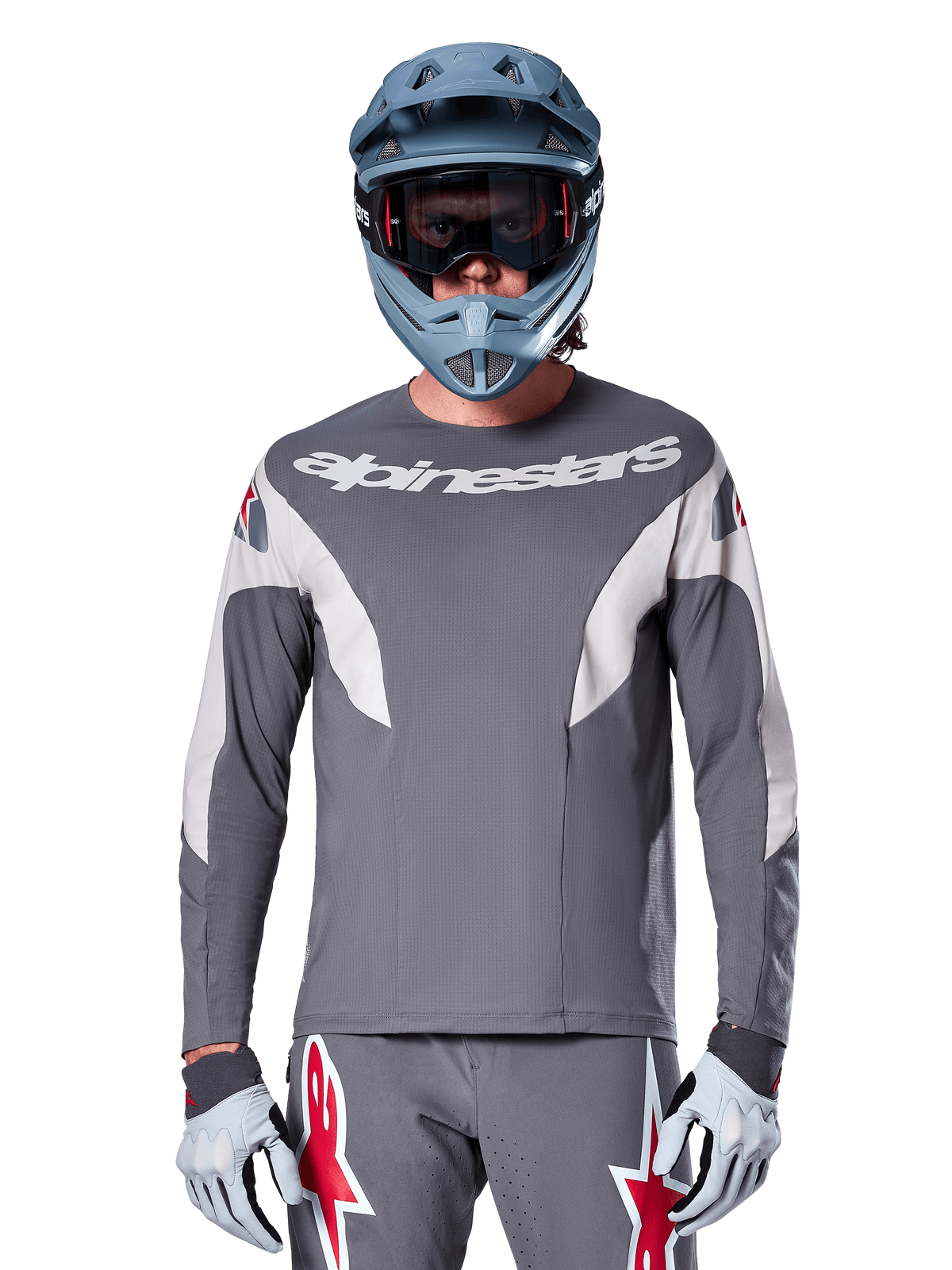 Pilote de VTT portant le maillot Alpinestars A-Supra Race - Manches longues en gris foncé, maillot de cyclisme à manches longues avec logo Alpinestars blanc, associé à un casque intégral gris-bleu, un masque et des gants de course gris, équipement de VTT complet pour la performance tout-terrain