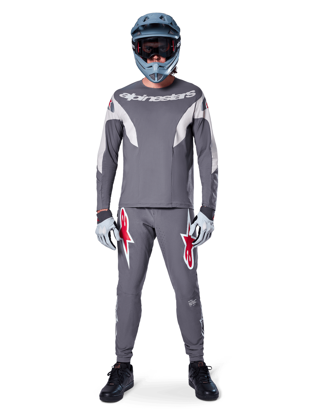 Pilote portant le maillot Alpinestars A-Supra Race - Manches longues en gris foncé, coordonné avec un pantalon gris assorti arborant des logos d'étoiles rouges, un casque gris avec lunettes et des gants gris clair, kit de VTT complet pour le cyclisme tout-terrain de performance