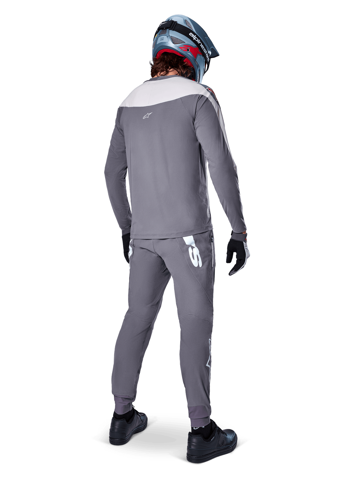 Maillot Alpinestars A-Supra Race, maillot de VTT à manches longues, gris foncé avec empiècement gris clair sur les épaules, vue de dos porté avec un pantalon assorti, casque intégral bleu et rouge, gants et chaussures noirs, équipement de cyclisme de performance inspiré par la course