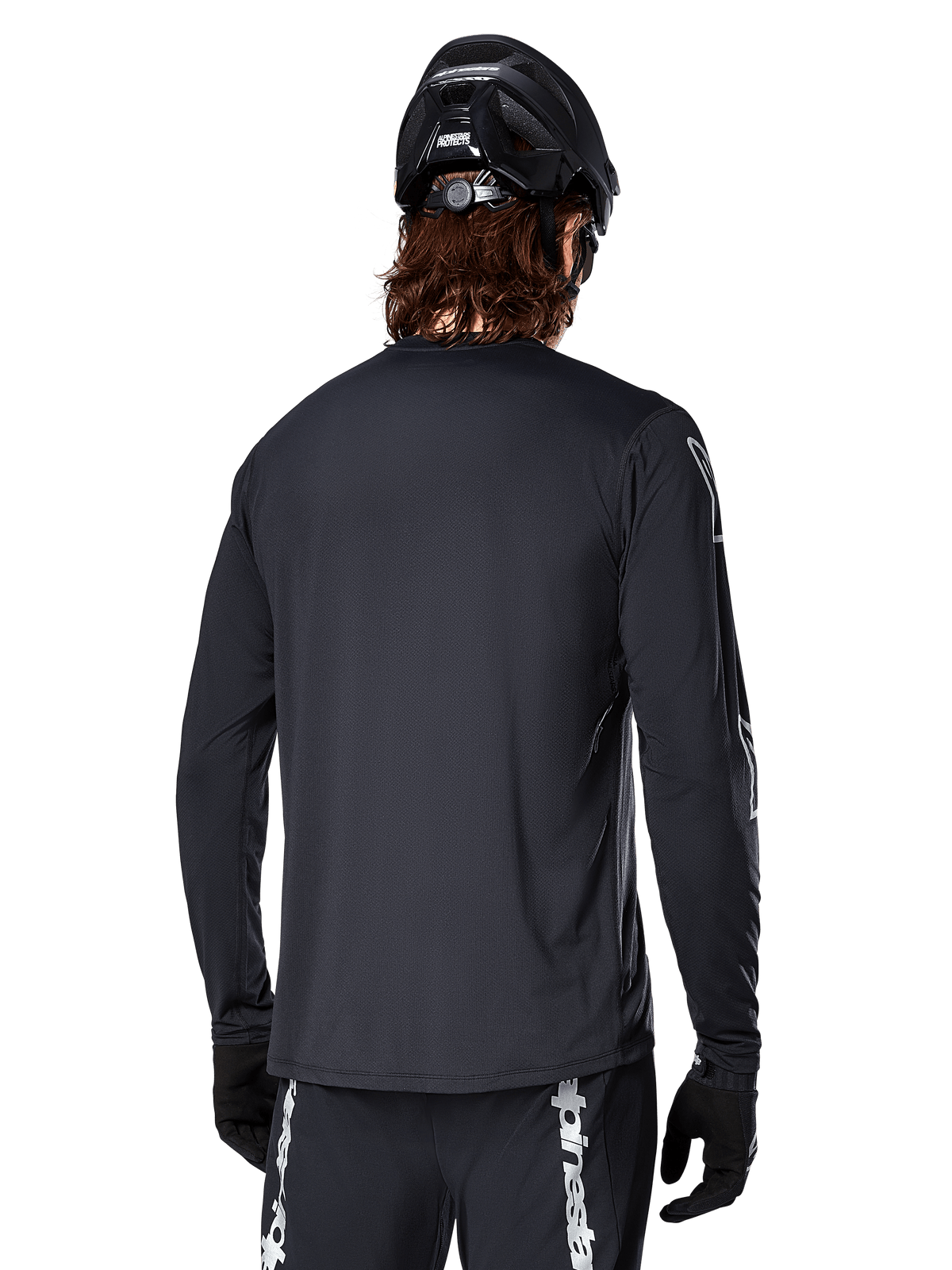 Alpinestars A-Dura Switch Jersey met lange mouwen, zwart, achteraanzicht van een fietser met zwarte MTB-helm en handschoenen, technisch jacquardweefsel en verlengde achterkant voor off-road rijden