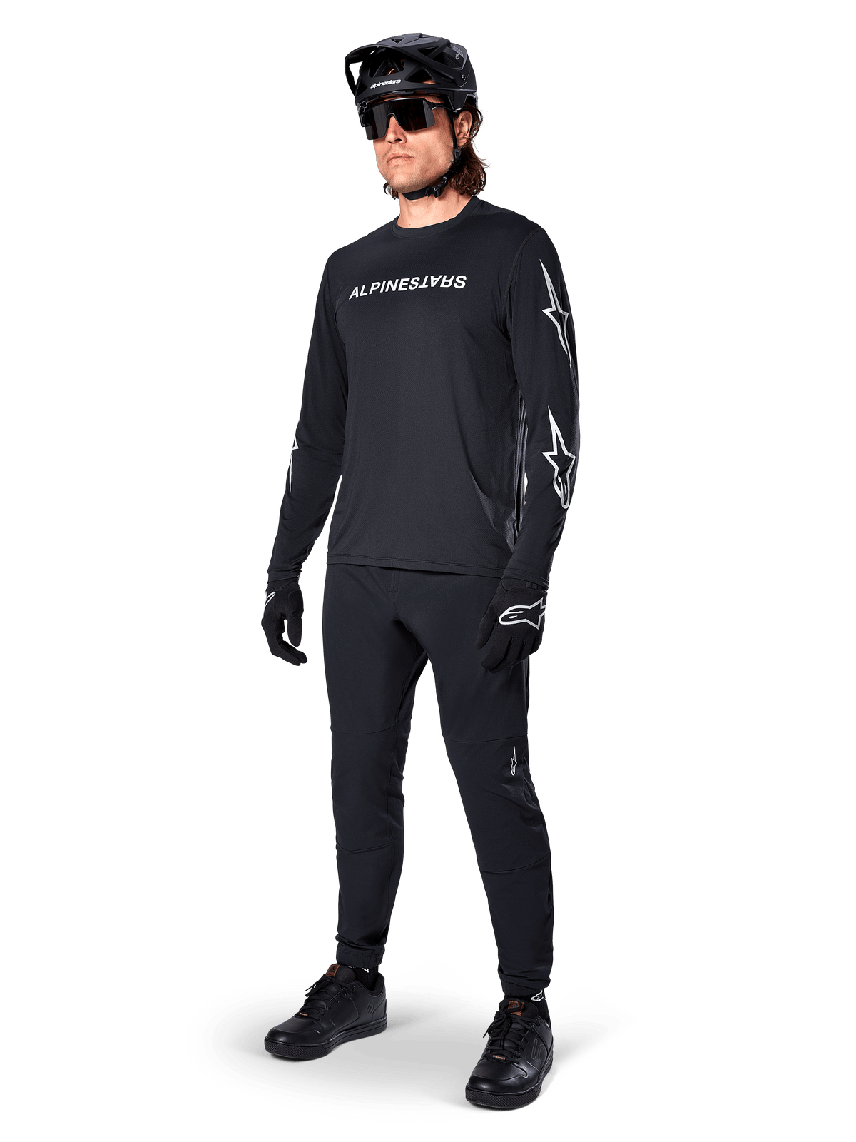 Alpinestars A-Dura Switch Jersey met lange mouwen, zwart, mountainbike jersey gedragen met zwarte broek, helm en handschoenen, voorzien van wit woordmerklogo op de borst en sterlogo's op de mouwen, gecoördineerde MTB-uitrusting voor off-road rijden