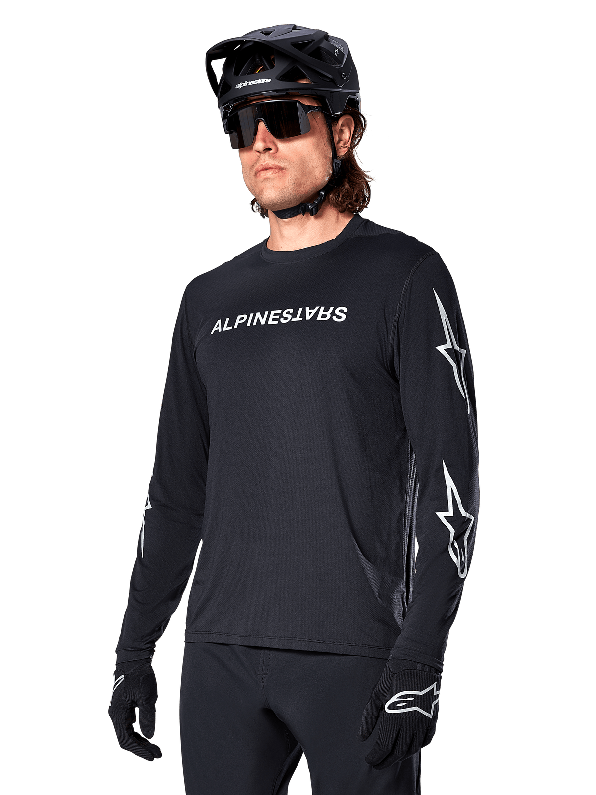 Mannelijke fietser draagt Alpinestars A-Dura Switch Jersey met lange mouwen, zwart met wit woordmerk en sterlogo's op de mouwen, gecombineerd met een zwarte MTB-helm en zonnebril, hoogwaardige fietskleding voor off-road rijden