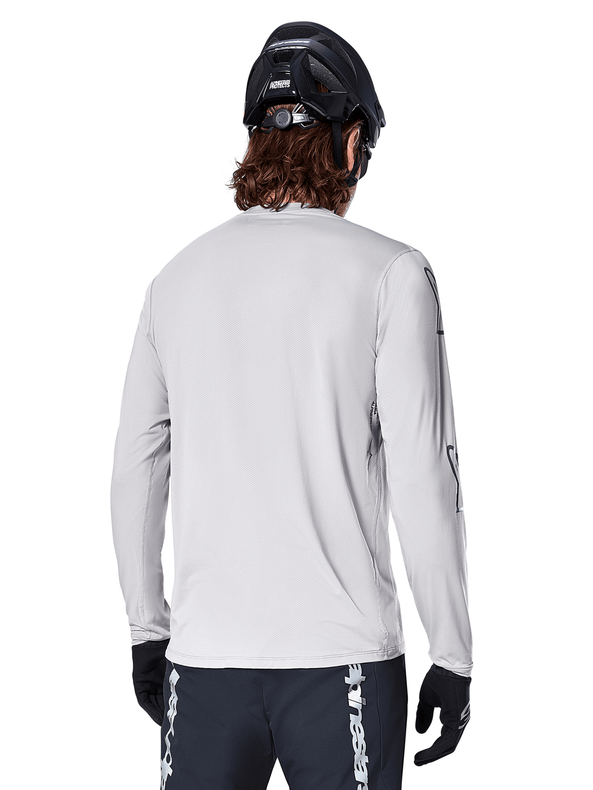 Alpinestars A-Dura Switch Long Sleeve Jersey, Light Gray, back view of a mountain biker wearing a black MTB helmet and gloves, featuring a drop tail for extra coverage and textured jacquard fabric, performance cycling gear.