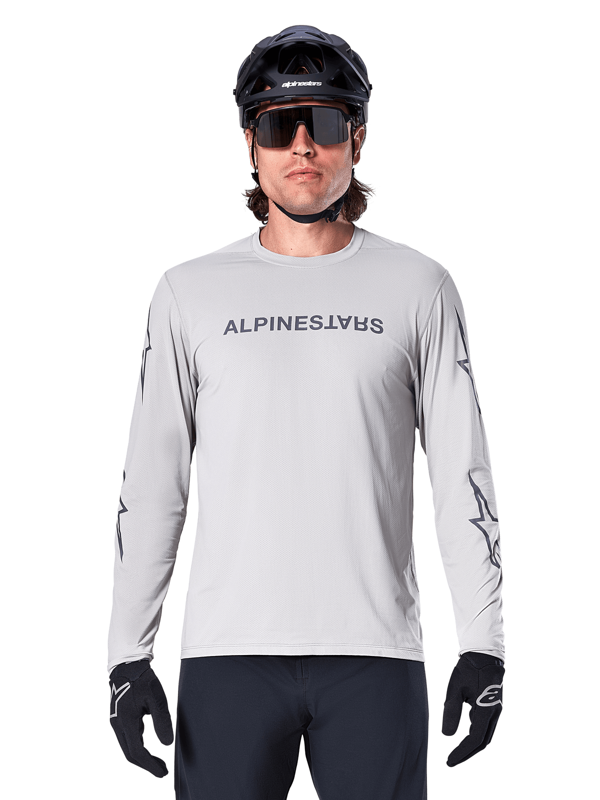Alpinestars A-Dura Switch Long Sleeve Jersey, Light Gray, features dark gray chest wordmark and sleeve star logos, worn by a rider with a black MTB helmet and gloves, performance cycling apparel for trail riding