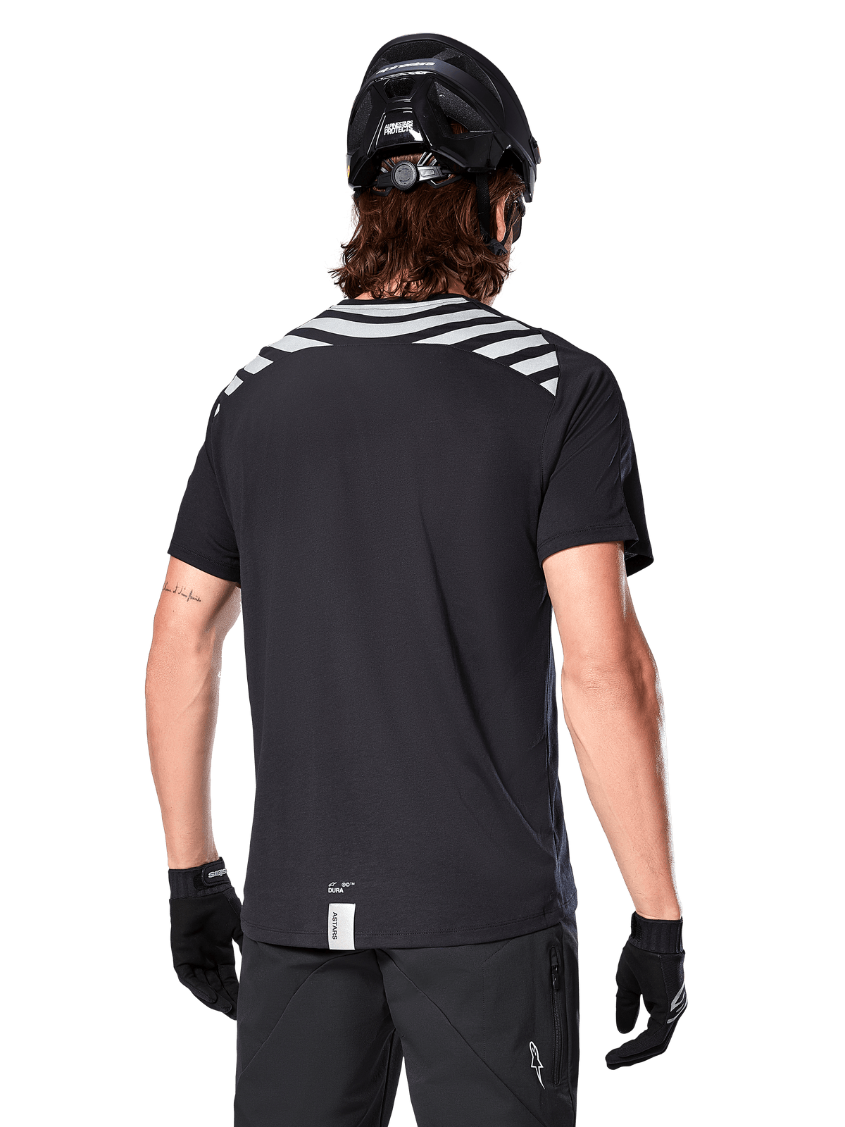 Maillot Alpinestars A-Dura Dri Oscar, maillot de VTT à manches courtes, noir réfléchissant, vue de dos sur mannequin portant un casque et des gants, bandes réfléchissantes grises aux épaules et dos rallongé, tissu technique évacuant l'humidité pour le VTT