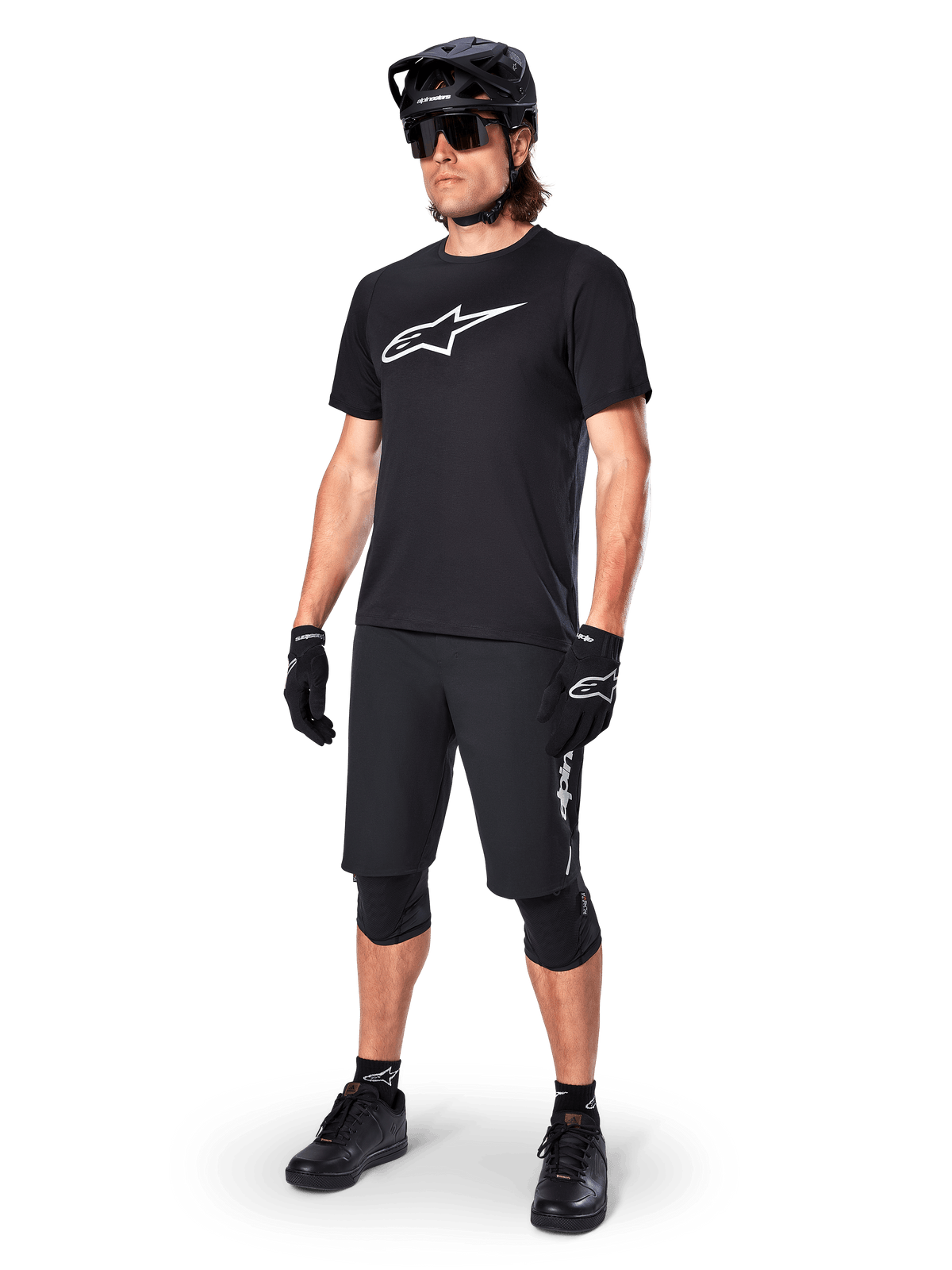 Mountainbike-Fahrer im Alpinestars A-Dura Dri Oscar Kurzarmtrikot in Schwarz Reflektierend, mit einem großen weißen Logo auf der Brust, kombiniert mit passenden schwarzen MTB-Shorts, Handschuhen und Helm, technische Radsportbekleidung für Offroad-Performance