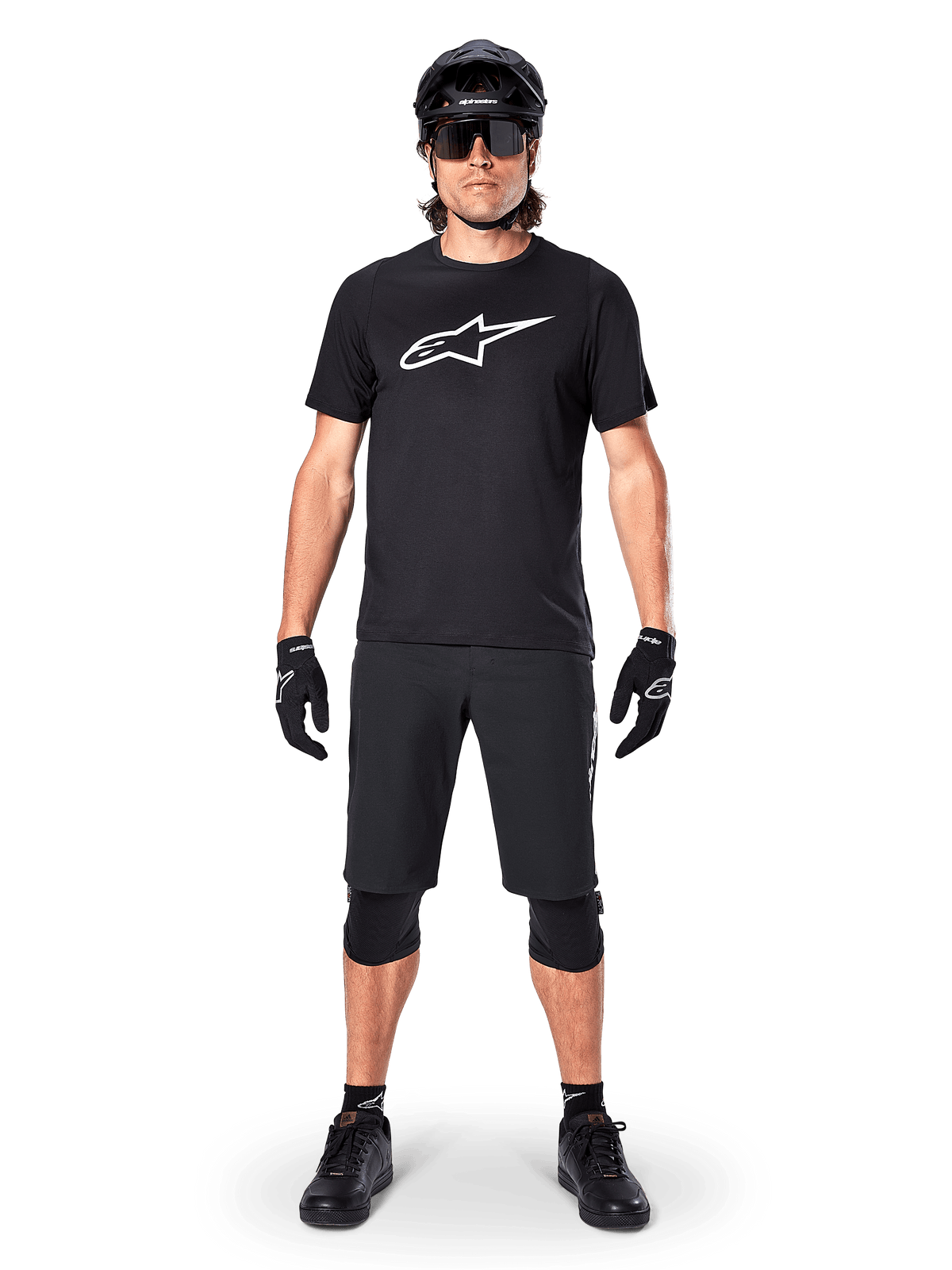 Alpinestars A-Dura Dri Oscar Kurzarmtrikot, Schwarz reflektierend, getragen mit passenden schwarzen MTB-Shorts, Handschuhen, Knieschützern und Helm, mit großem weißem Alpinestars-Logo auf der Brust, komplettes Mountainbike-Outfit