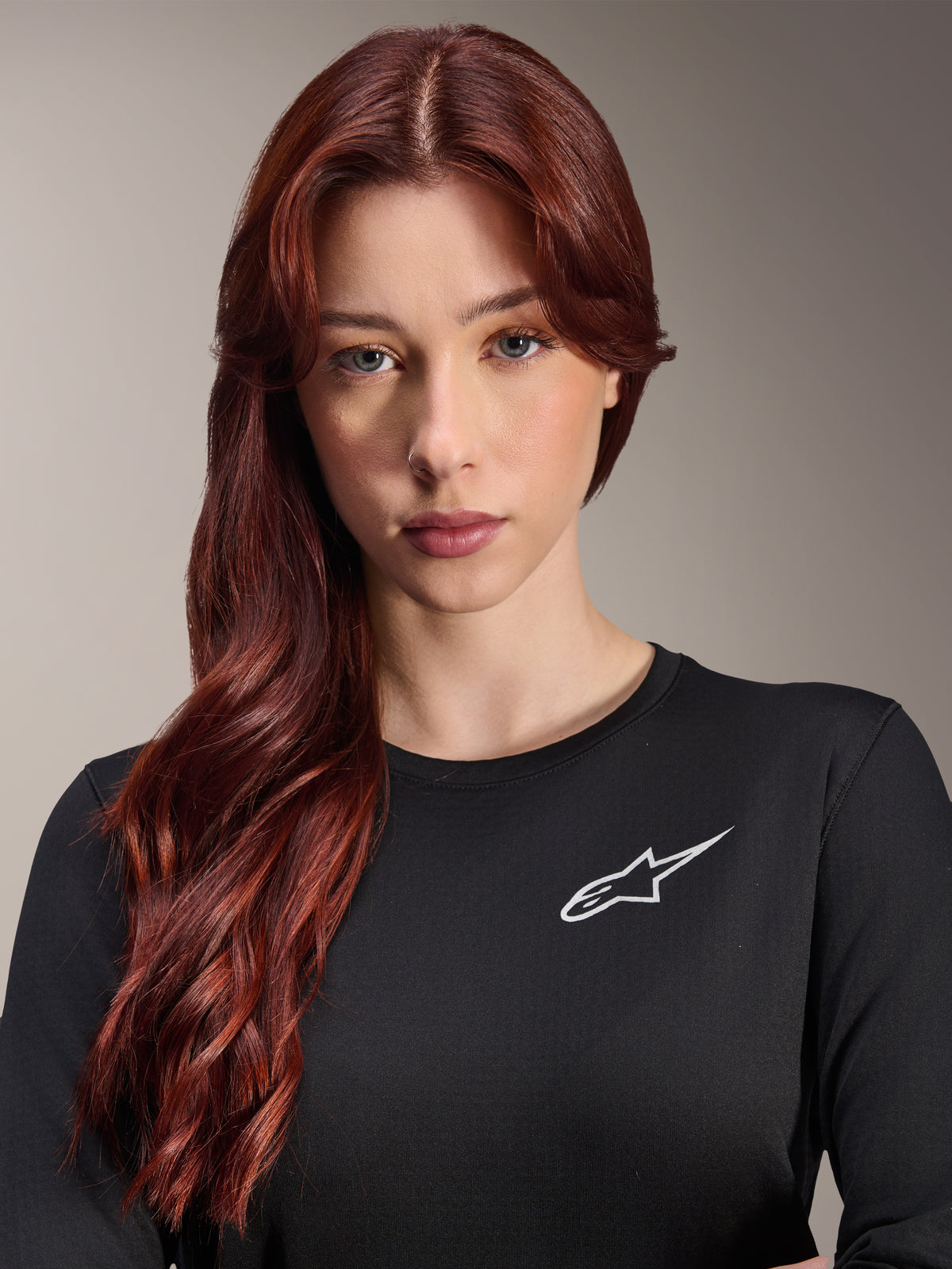 Maillot thermique Alpinestars Stella A-Dura, maillot de VTT à manches longues pour femme, noir avec logo A-star blanc sur la poitrine, portrait rapproché d'une femme aux longs cheveux roux, vêtement de cyclisme pour temps frais