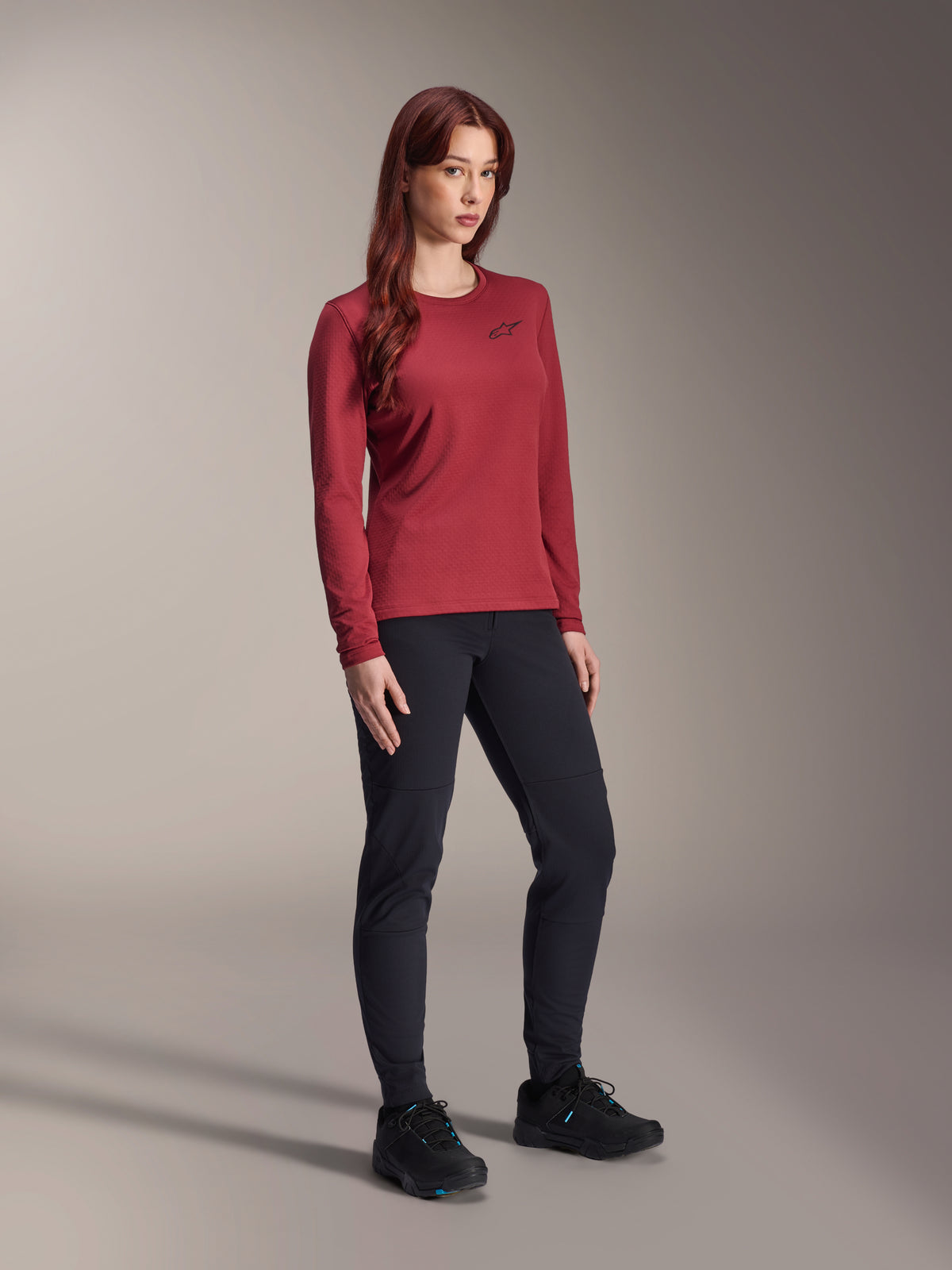 Alpinestars Stella A-Dura Thermal Jersey, mountainbike-jersey voor dames met lange mouwen, burgundy, gedragen met een zwarte sportbroek en zwarte schoenen, ronde hals met een klein zwart logo op de borst, functioneel ontwerp met normale pasvorm voor off-road fietsen