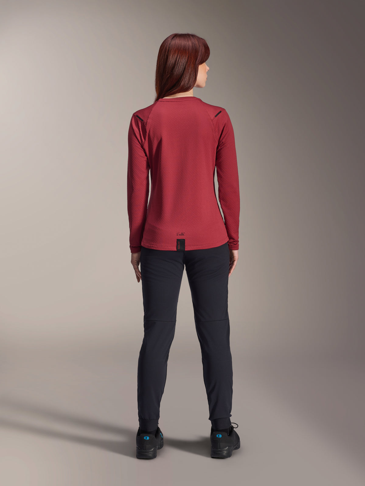 Alpinestars Stella A-Dura Thermal broek, mountainbikebroek voor dames, zwart, gedragen met een bordeauxrode jersey met lange mouwen, achteraanzicht dat de technische pasvorm en constructie voor fietsen in koud weer toont.