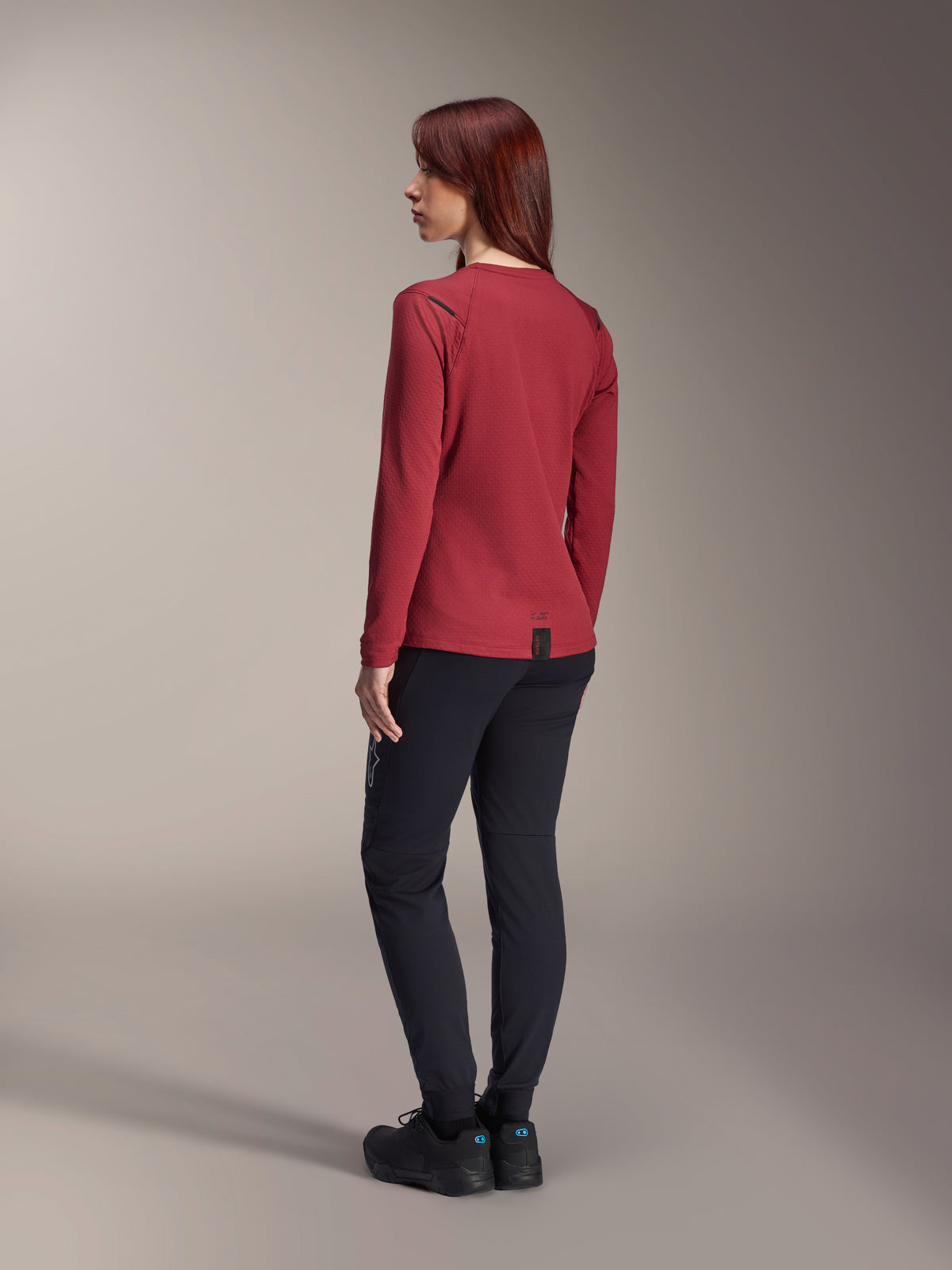 Vrouw draagt Alpinestars Stella A-Dura Thermal broek in zwart, gecombineerd met een rode thermische jersey met lange mouwen en zwarte schoenen, achteraanzicht, mountainbikekleding voor ritten in koud weer.