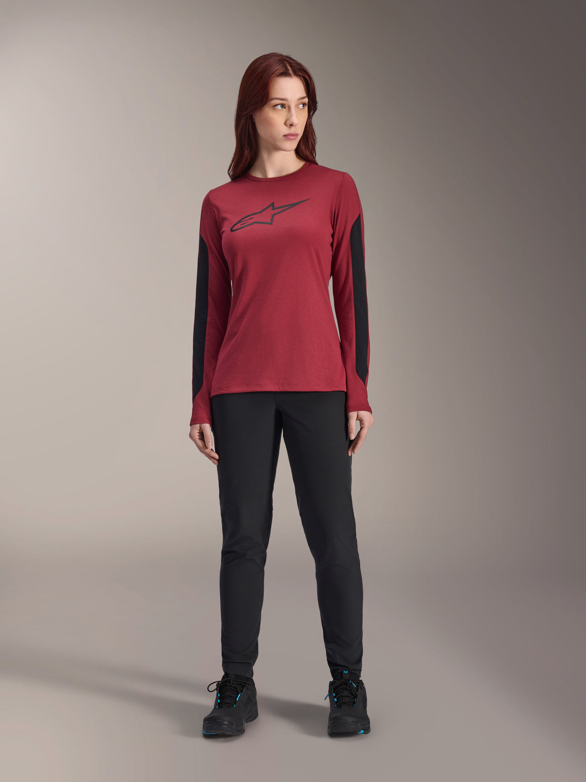 Alpinestars Women Stella A-Dura Dri Astar Long Sleeve Jersey in Burgundy, featuring a black Astars logo on the chest and black mesh arm panels, styled with black technical pants and athletic shoes, performance mountain bike apparel for women.