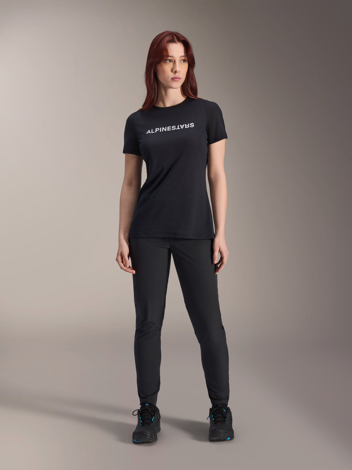 Alpinestars Stella A-Dura Dri Switch Kurzarmtrikot für Damen in Schwarz, weißes Logo-Branding auf der Brust, kombiniert mit schwarzer technischer Hose und schwarzen Sportschuhen, Ganzkörper-Studioaufnahme.