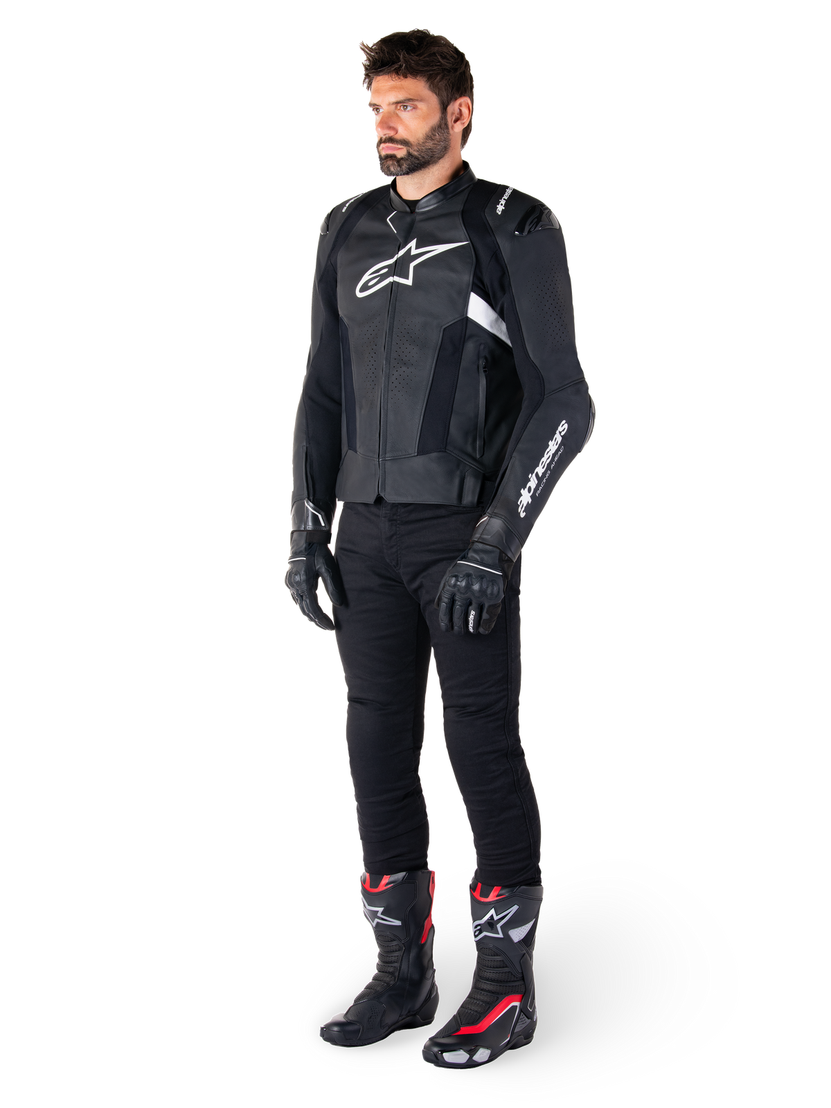 Mannelijke motorrijder die de Alpinestars Missile V3 lederen jas in het zwart en wit draagt, voorzien van een wit logo op de borst en geperforeerde lederen panelen, gecombineerd met een zwarte motorbroek, zwarte handschoenen en zwart-rode racelaarzen voor een complete sportieve motoroutfit.