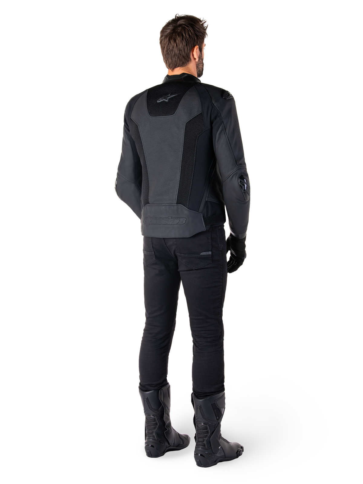 Achteraanzicht van een man die de Alpinestars Missile V3 Airflow leren jas in het zwart draagt, voorzien van uitgebreide geperforeerde panelen voor ventilatie, gecombineerd met een zwarte motorbroek en laarzen, met een gestroomlijnde race-esthetiek.