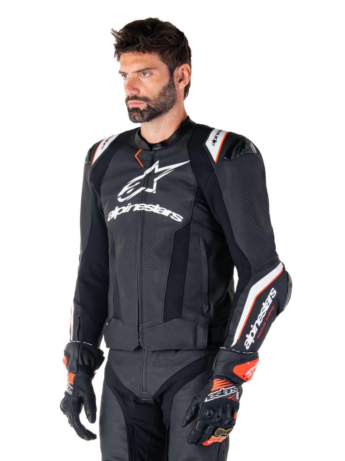 Mannelijk model in de Alpinestars Missile V3 Ignition leren jas, zwart met witte en oranje accenten, voorzien van opvallende witte logo's, geperforeerde leren delen en beschermende schouderprotectie, gestyled met racehandschoenen voor een sportieve race-look.
