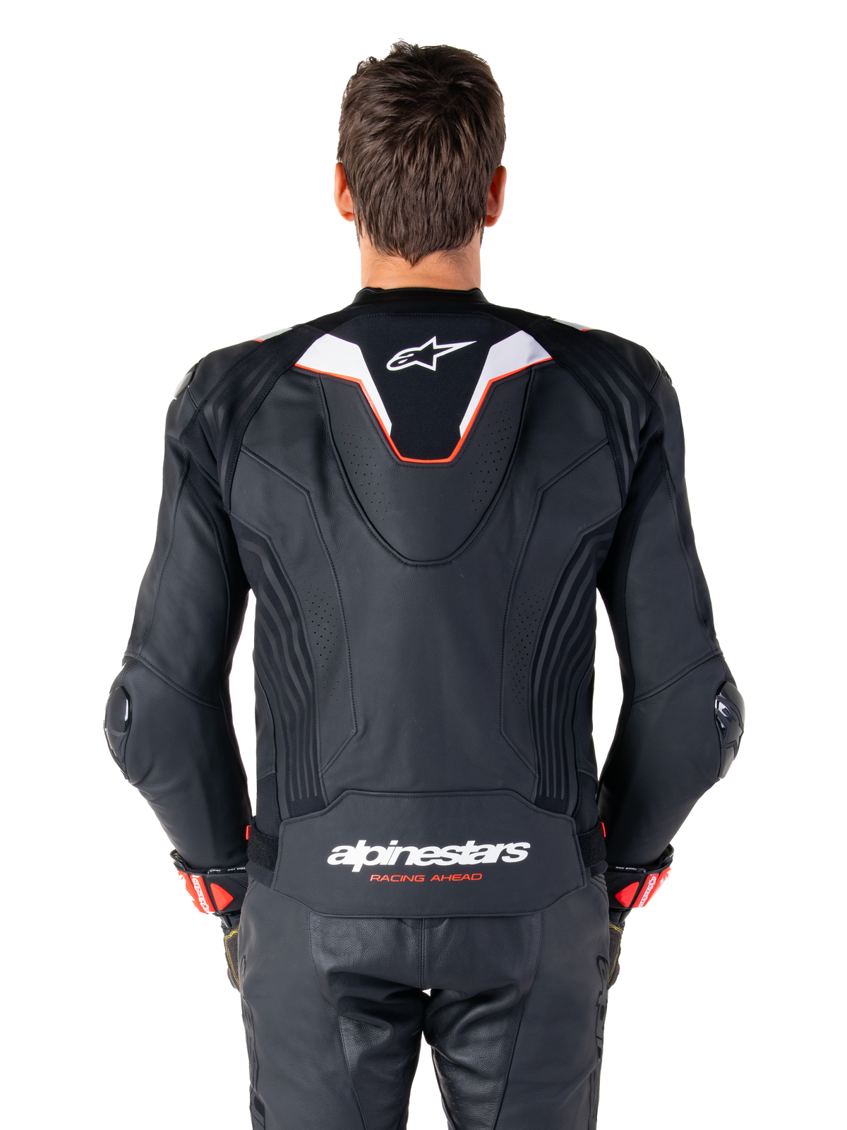 Alpinestars Missile V3 Ignition leren jas, achteraanzicht van een motorrijder, zwart leer met witte en rode accenten, voorzien van een slanke sport aero-hump met wit logo en 'alpinestars RACING AHEAD' branding op de onderrug, gecombineerd met bijpassende zwarte leren racebroek en handschoenen.